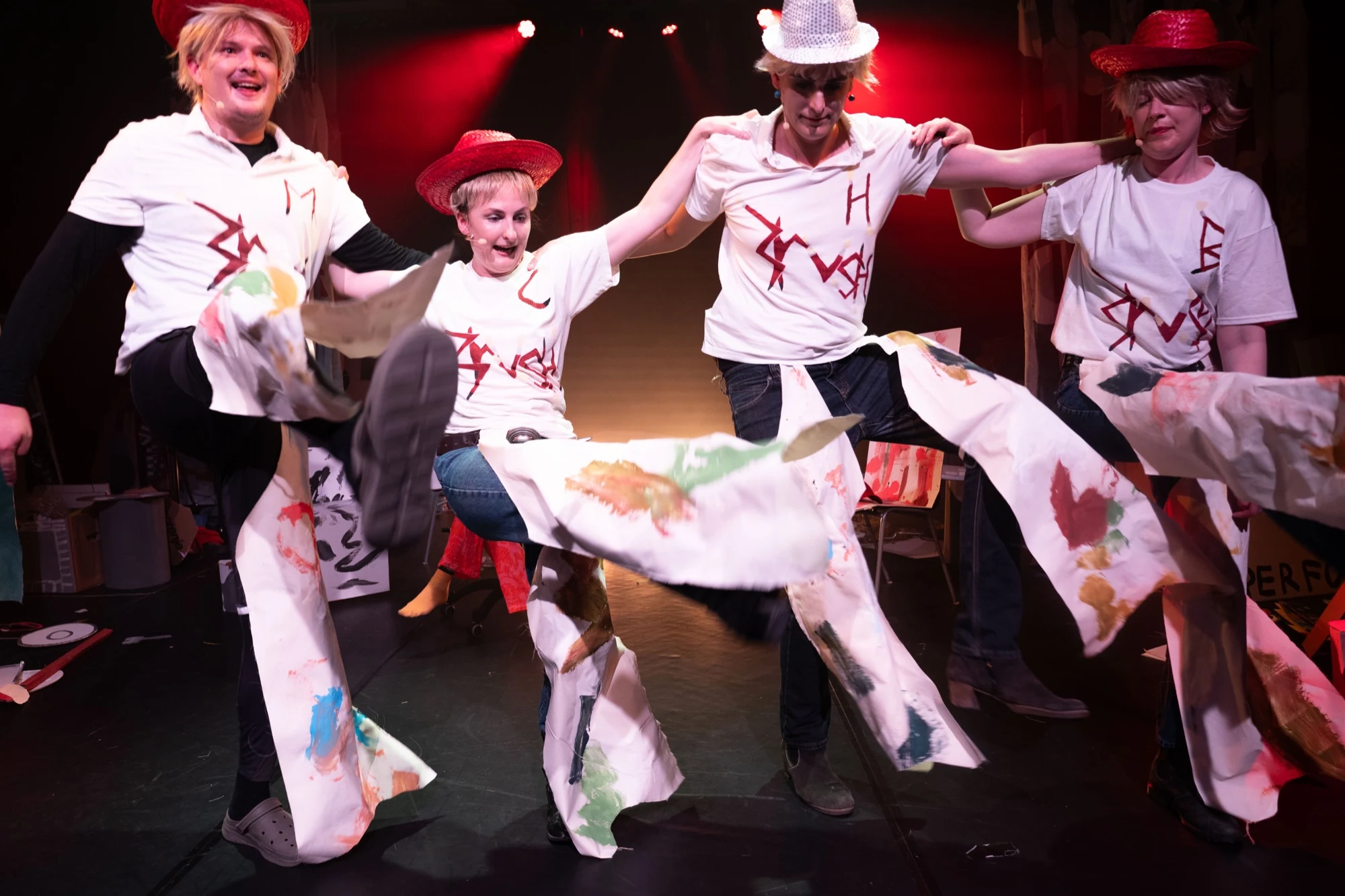 Four performers in sparkling hats dancing with linked arms.