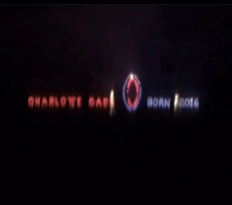 A firework display spelling Charlotte Gash and Born 2016 on a dark rugby field.