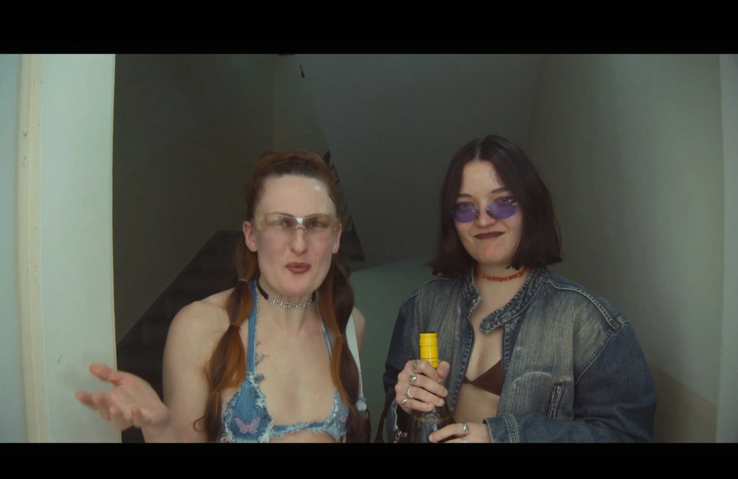 Two characters wearing tinted glasses standing in a doorway, one holding a bottle.