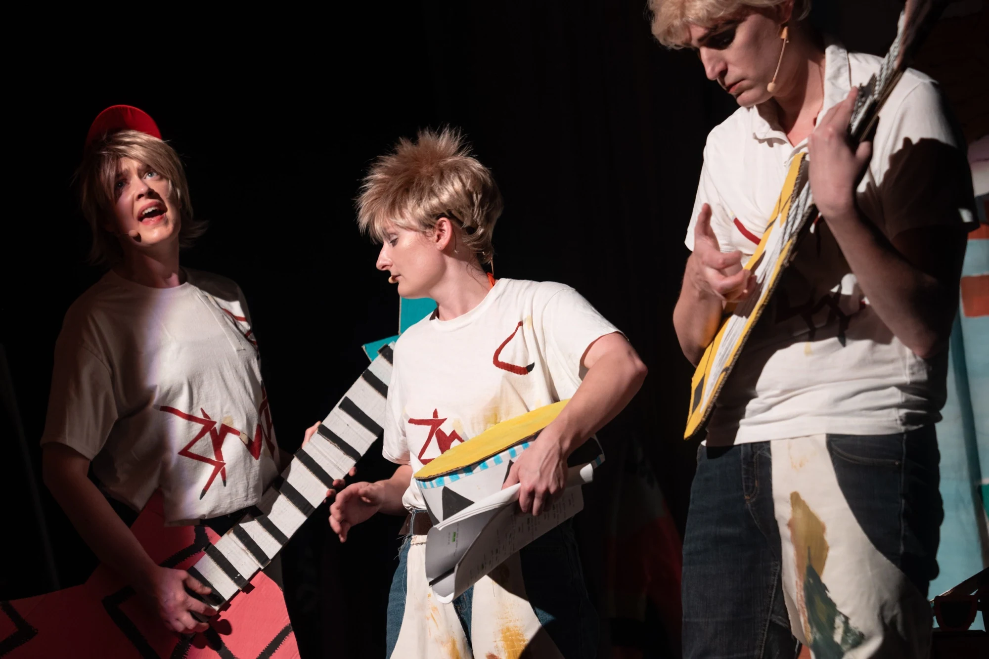 Three performers holding handmade cardboard guitars and a drum.