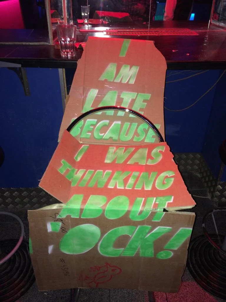 A cardboard dress with green lettering displayed on a bar stool.