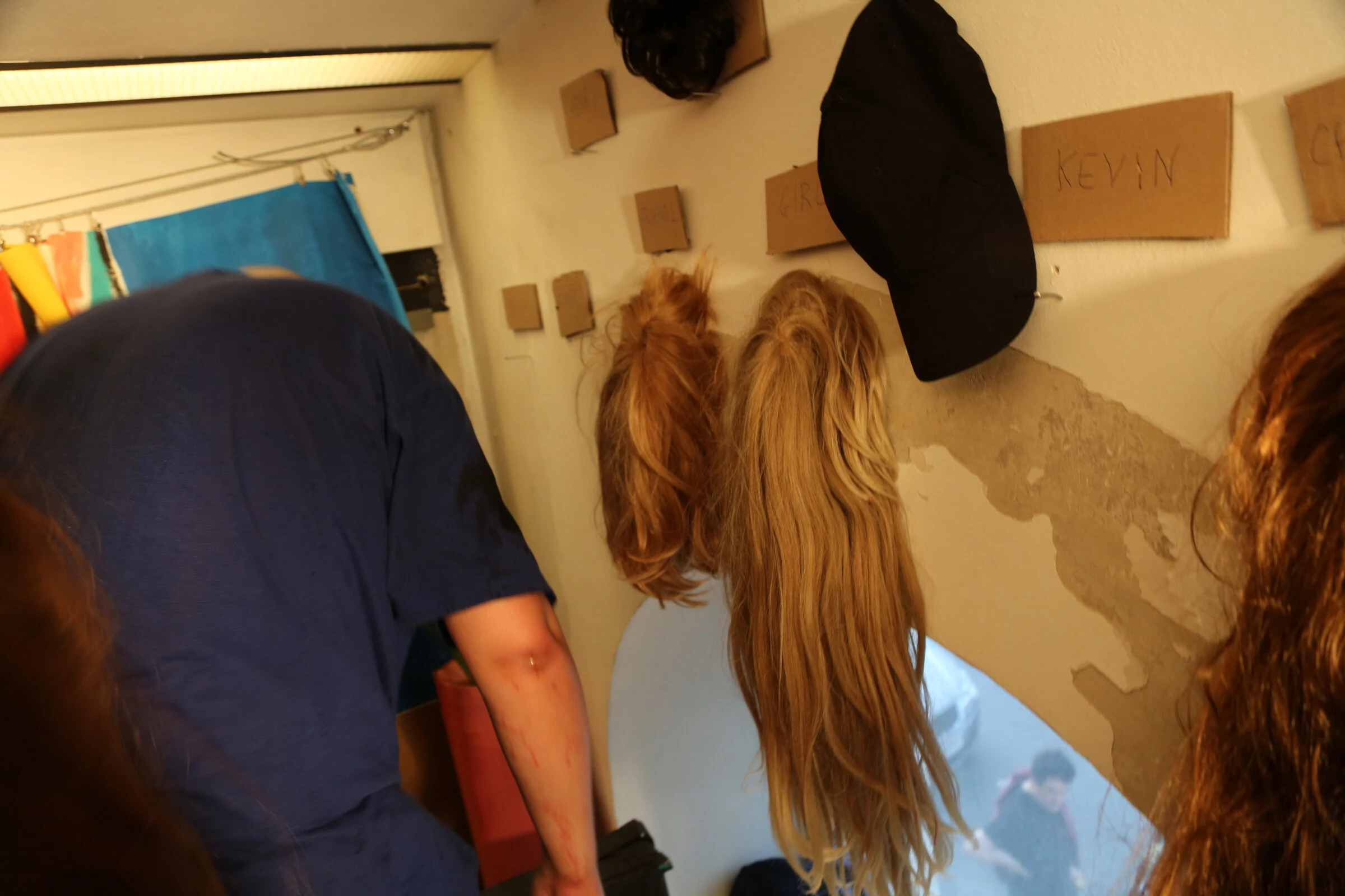 Wigs and a black cap hanging beside cardboard character labels during the performance.