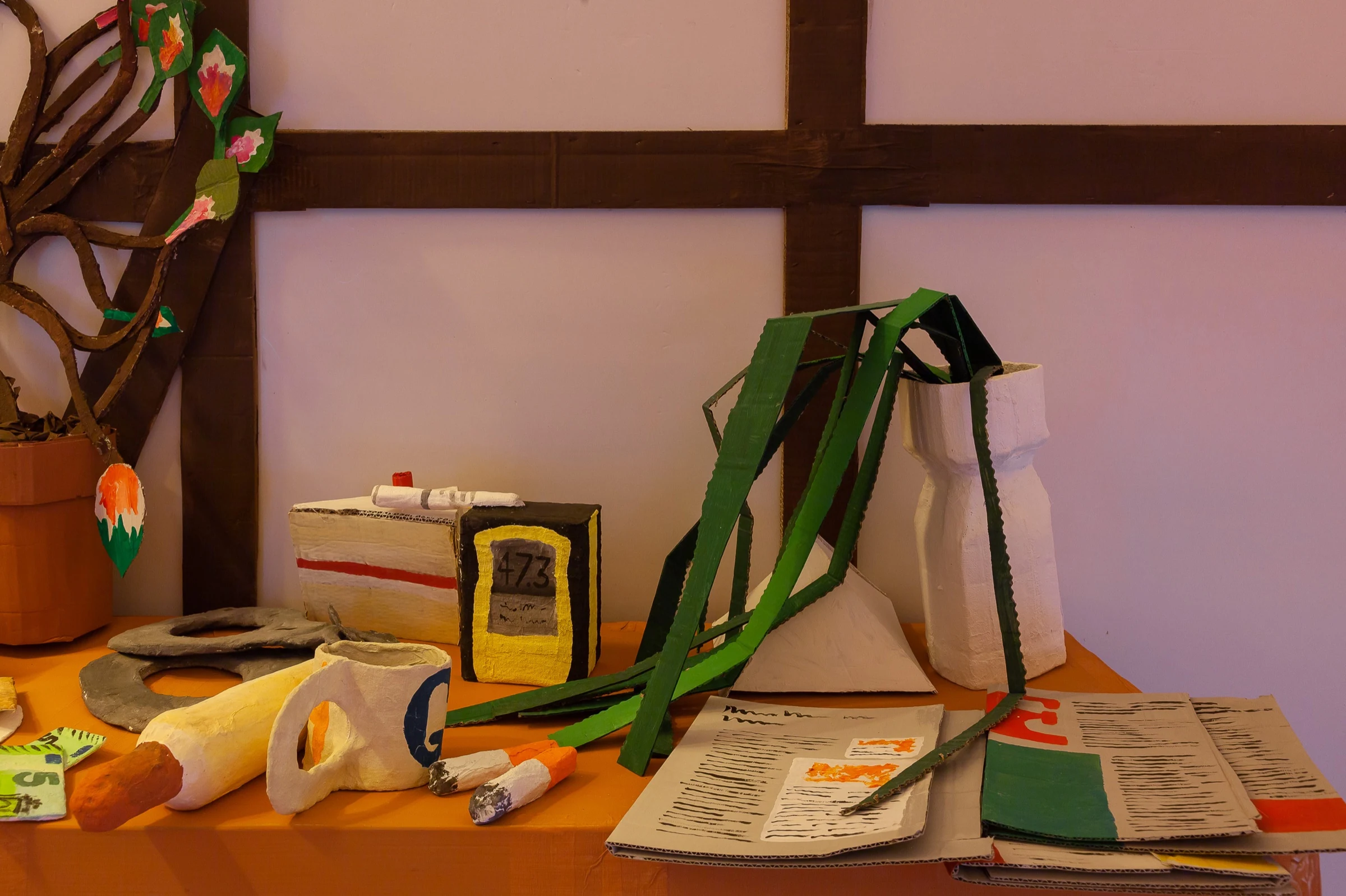 A tabletop filled with handmade cardboard food, books and kitchen objects.