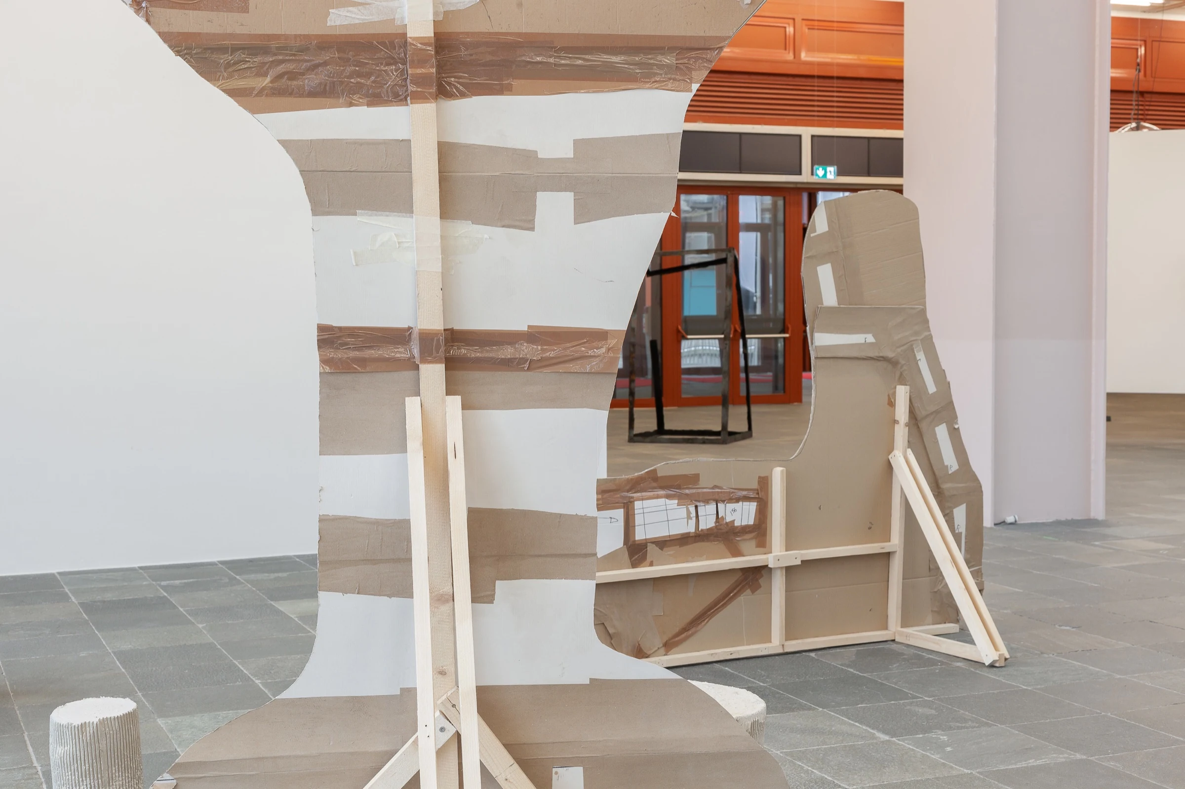 The taped cardboard and wooden supports behind the oversized cocktail glass sculpture.