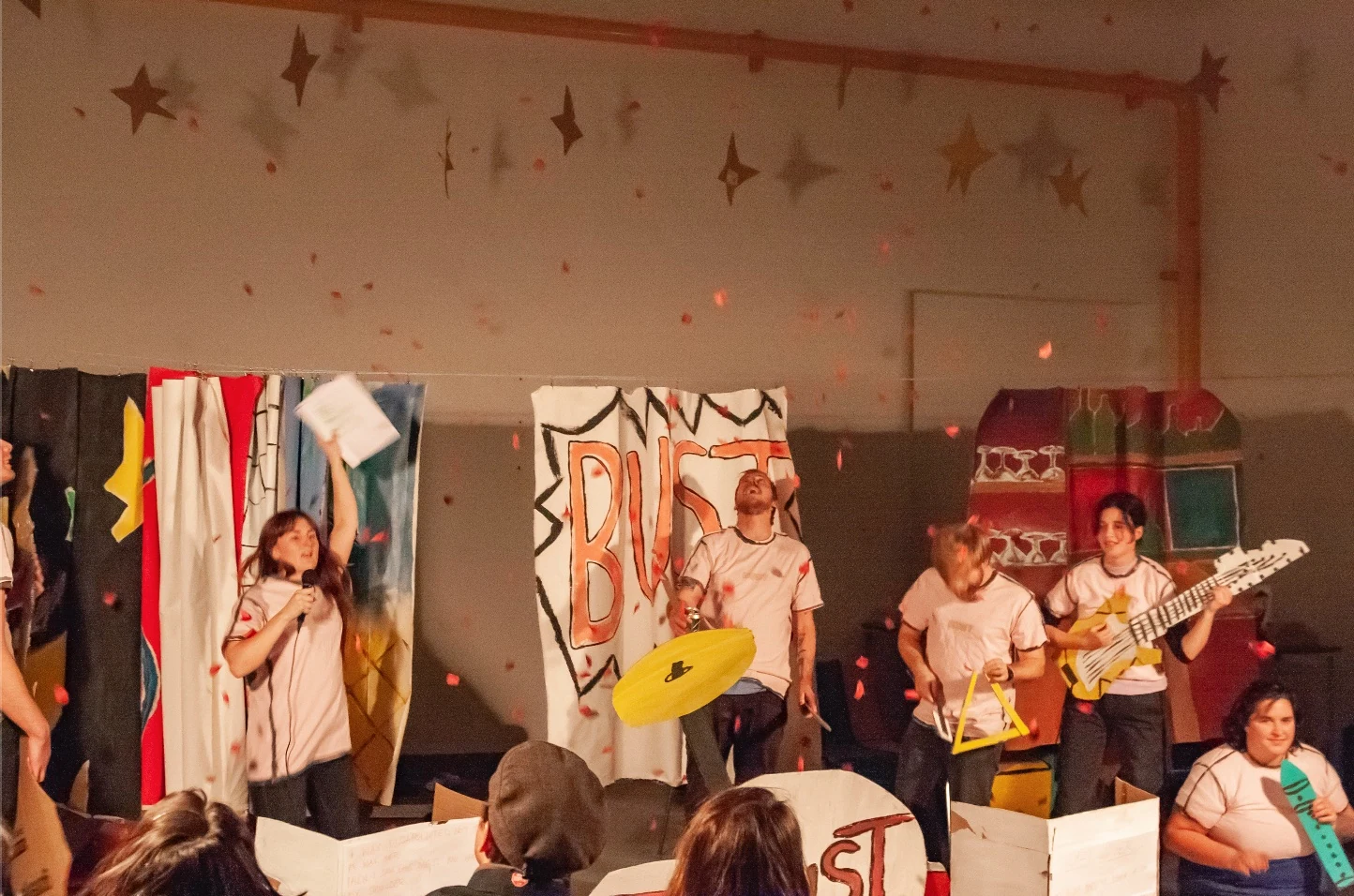 Performers playing cardboard instruments as confetti falls over the stage.