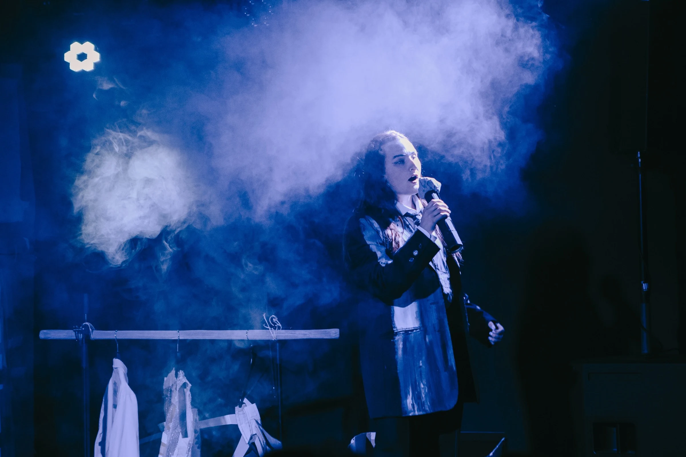 Charlotte Gash singing into a microphone surrounded by blue stage light and smoke.