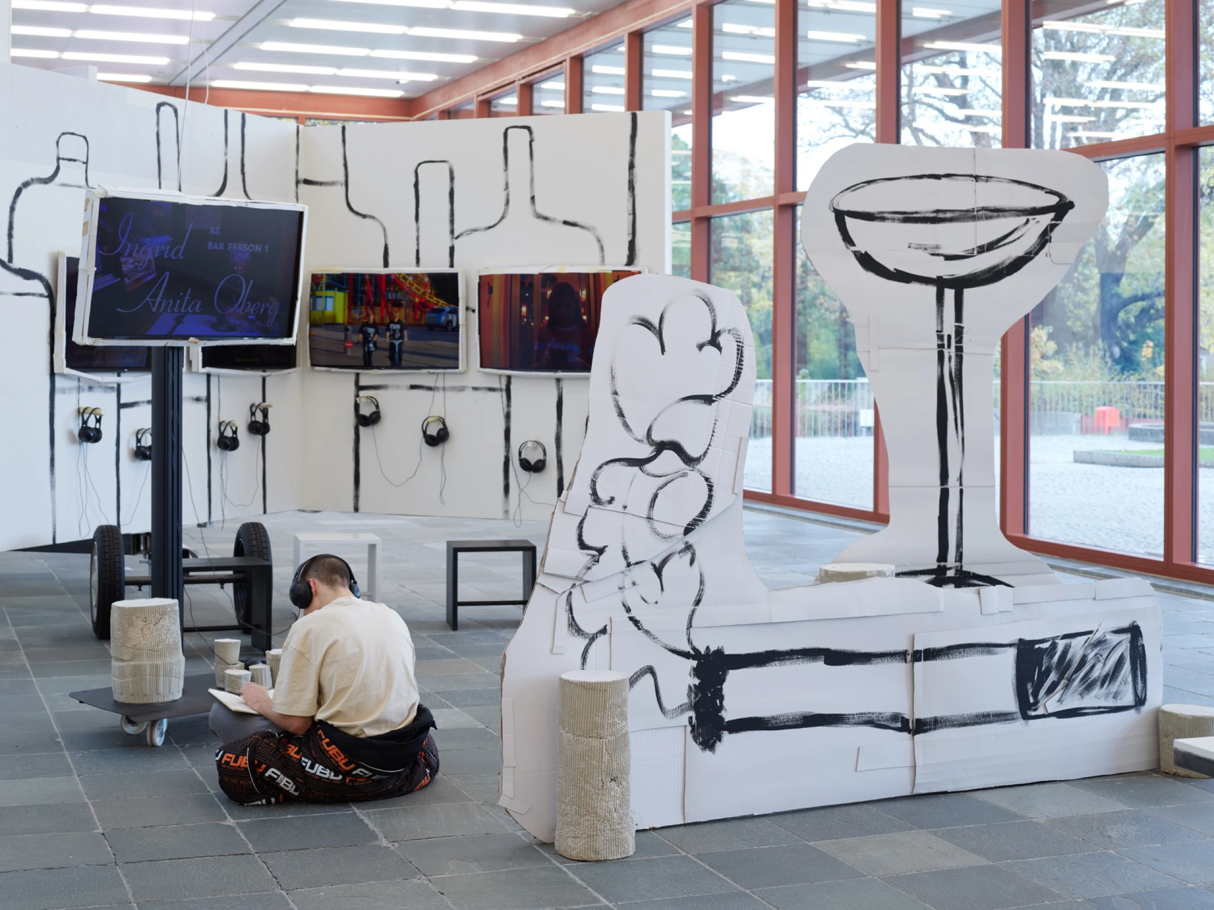 A seated visitor wearing headphones in front of the Location video installation.