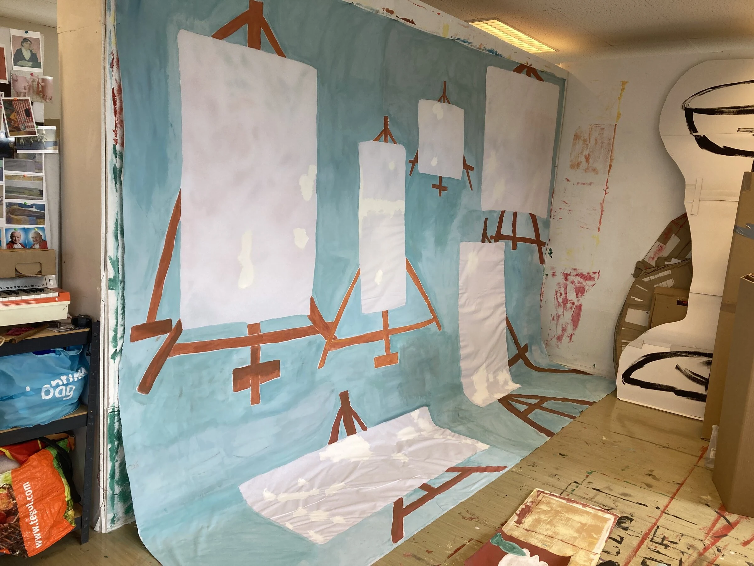 A pale blue backdrop depicting blank canvases on wooden easels in the studio.