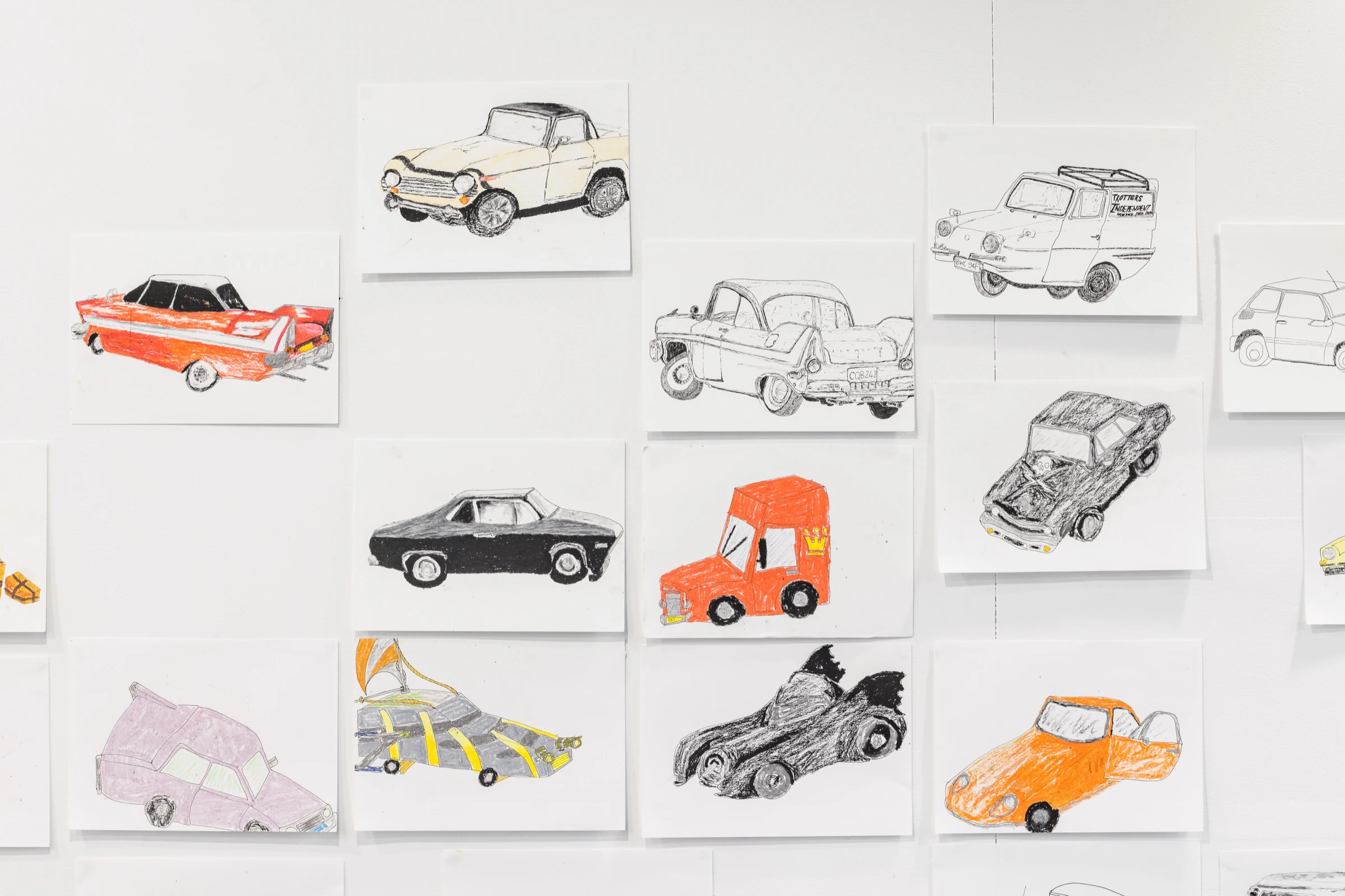 A gallery wall displaying drawings of cars in pencil and coloured crayon.