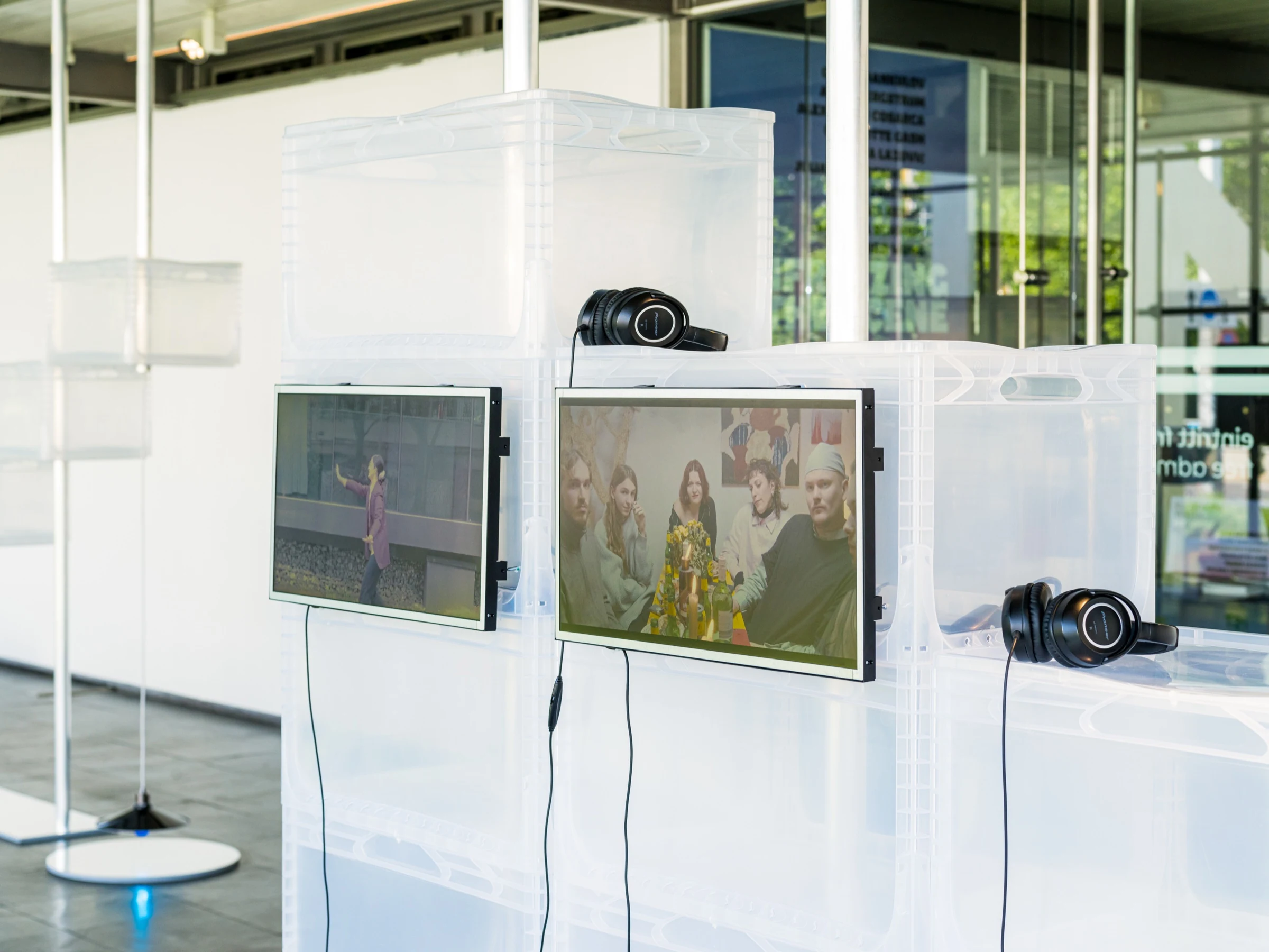 Two video screens and headphones mounted on stacks of transparent crates.