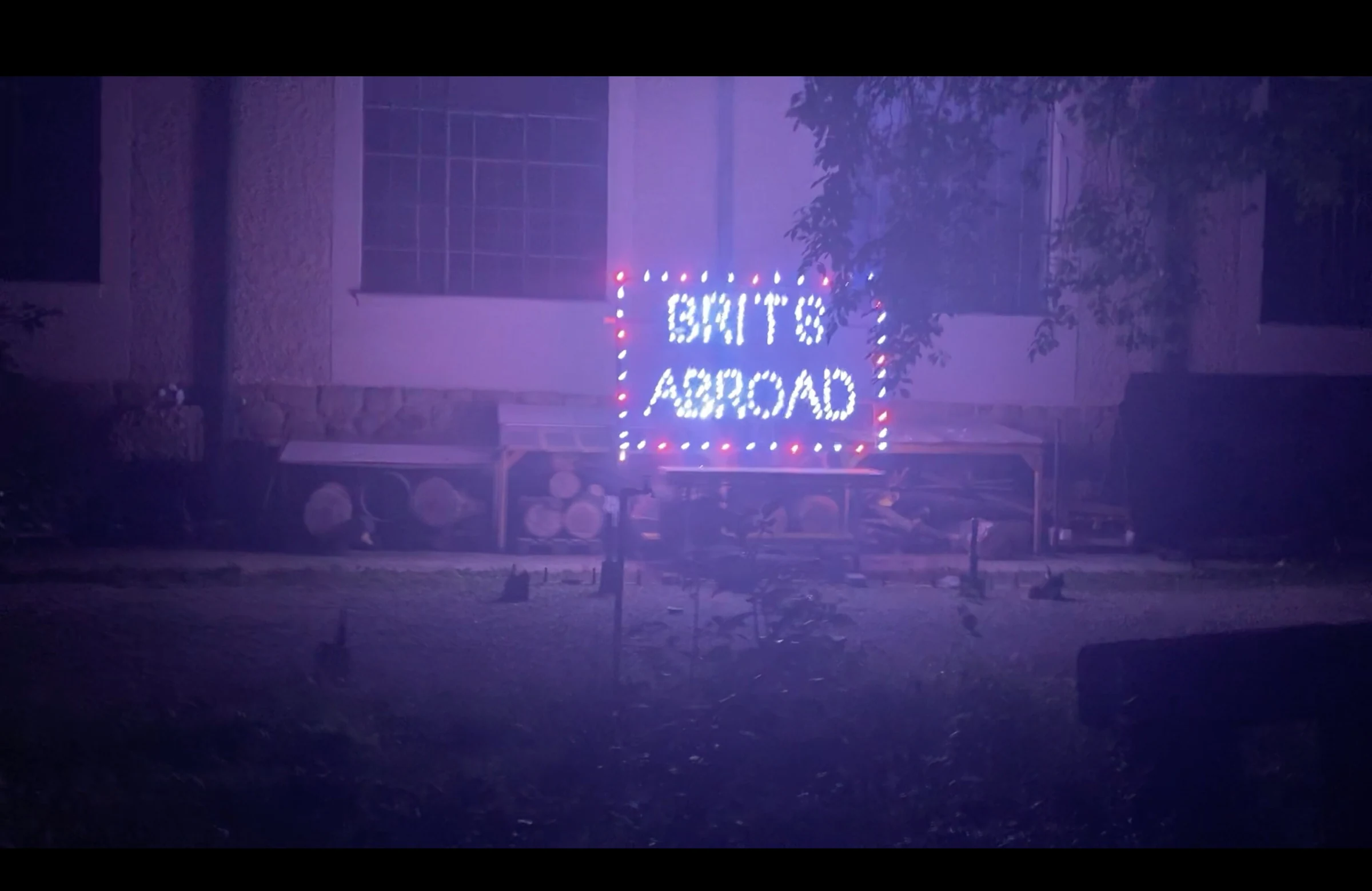 A wide view of the illuminated BRITS ABROAD sign in a smoky courtyard.