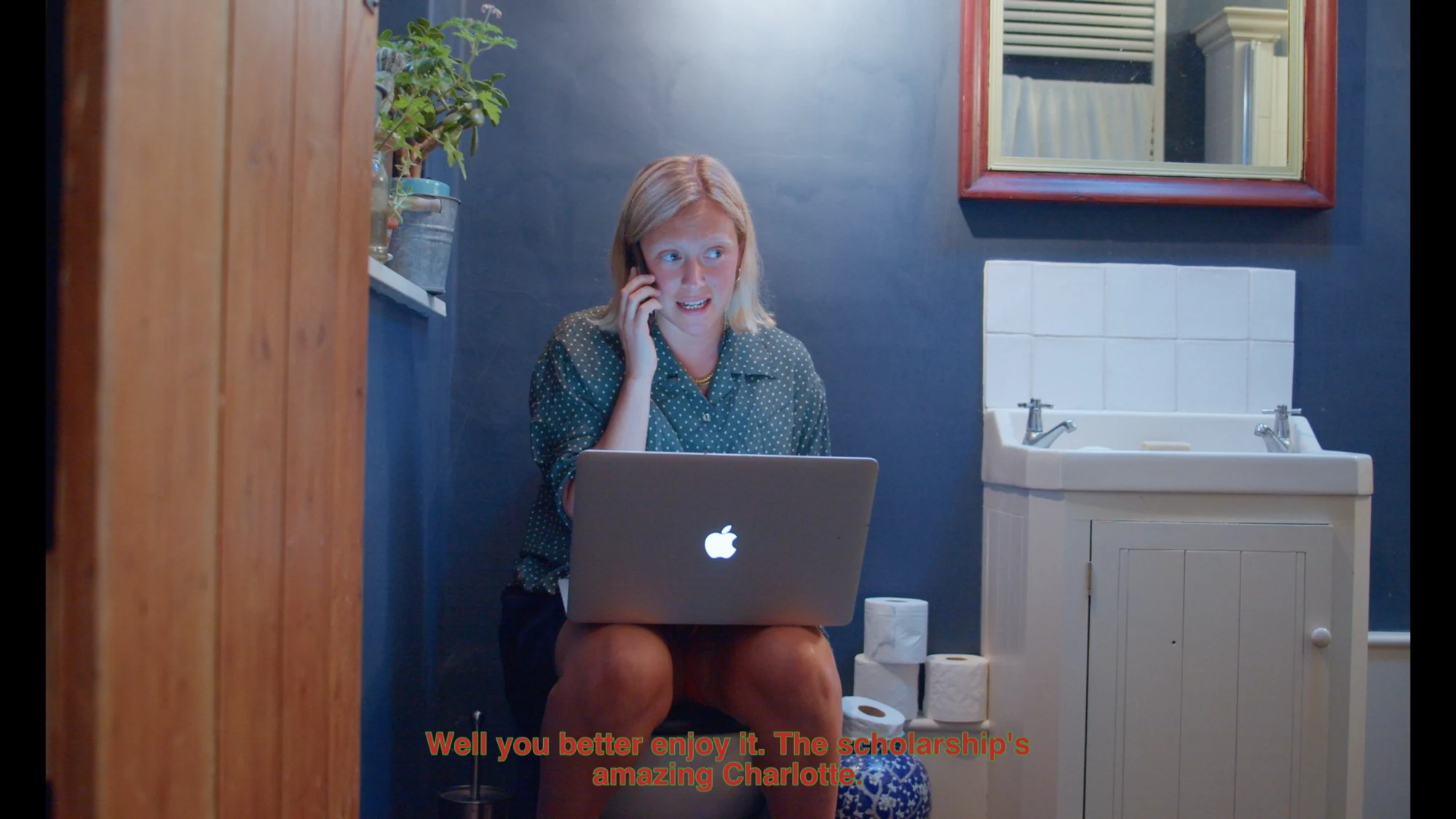 A woman on the phone with a laptop in a blue bathroom.