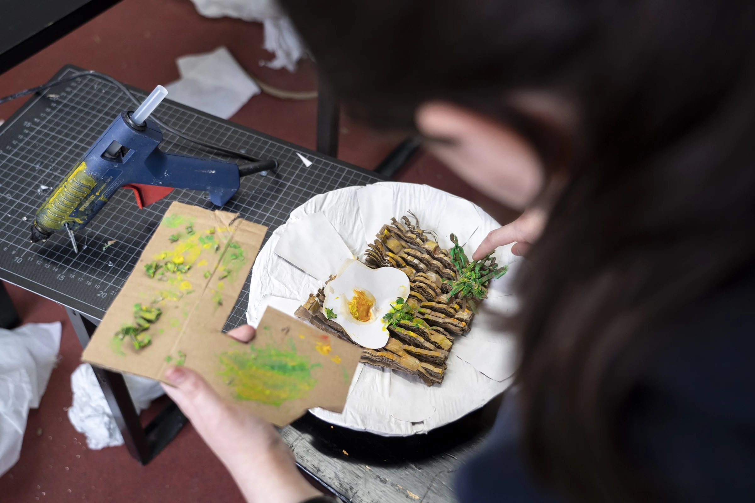 A participant assembling a cardboard meal with noodles, greens and a fried egg.