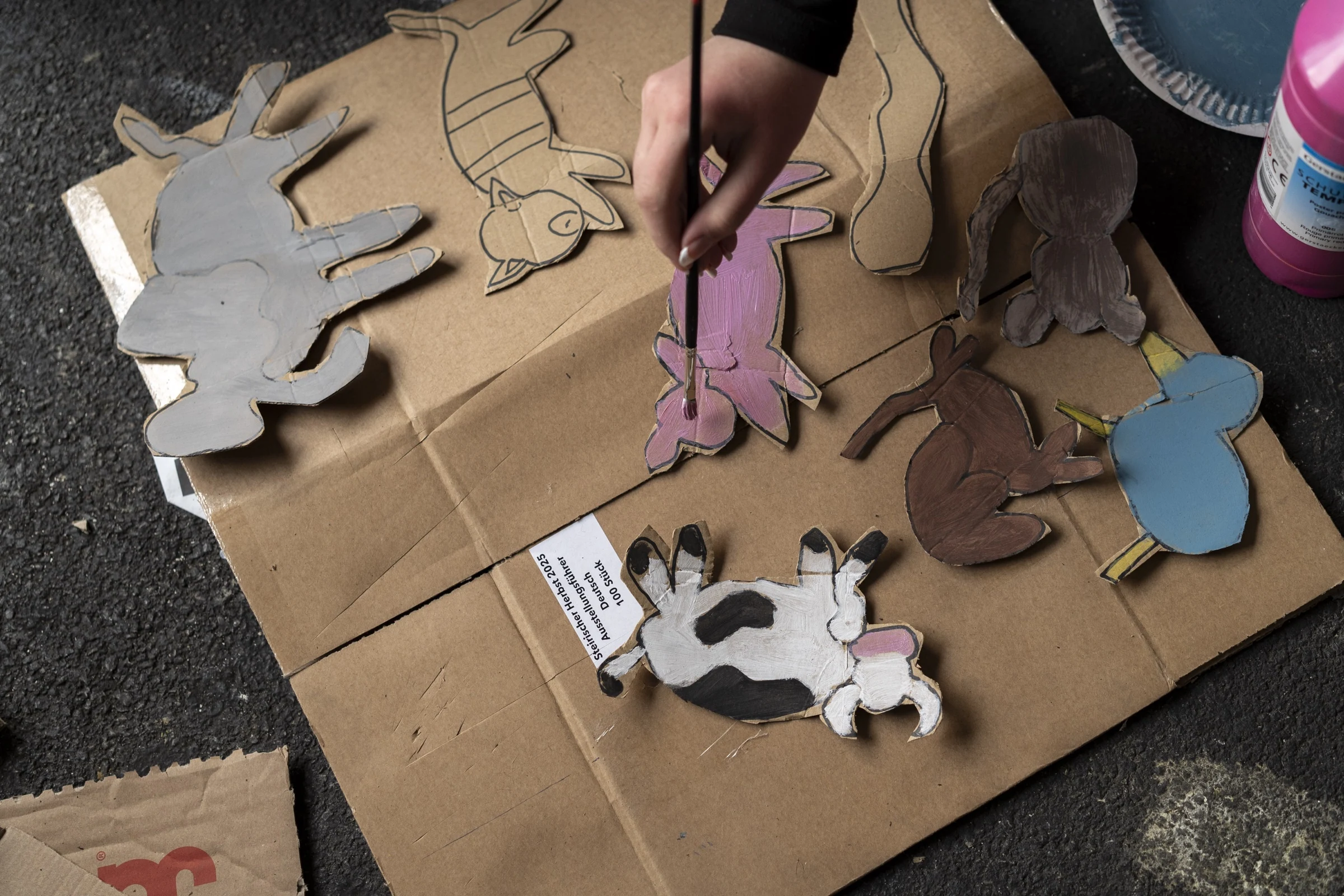 A participant painting a pink cat among cardboard animal cutouts.