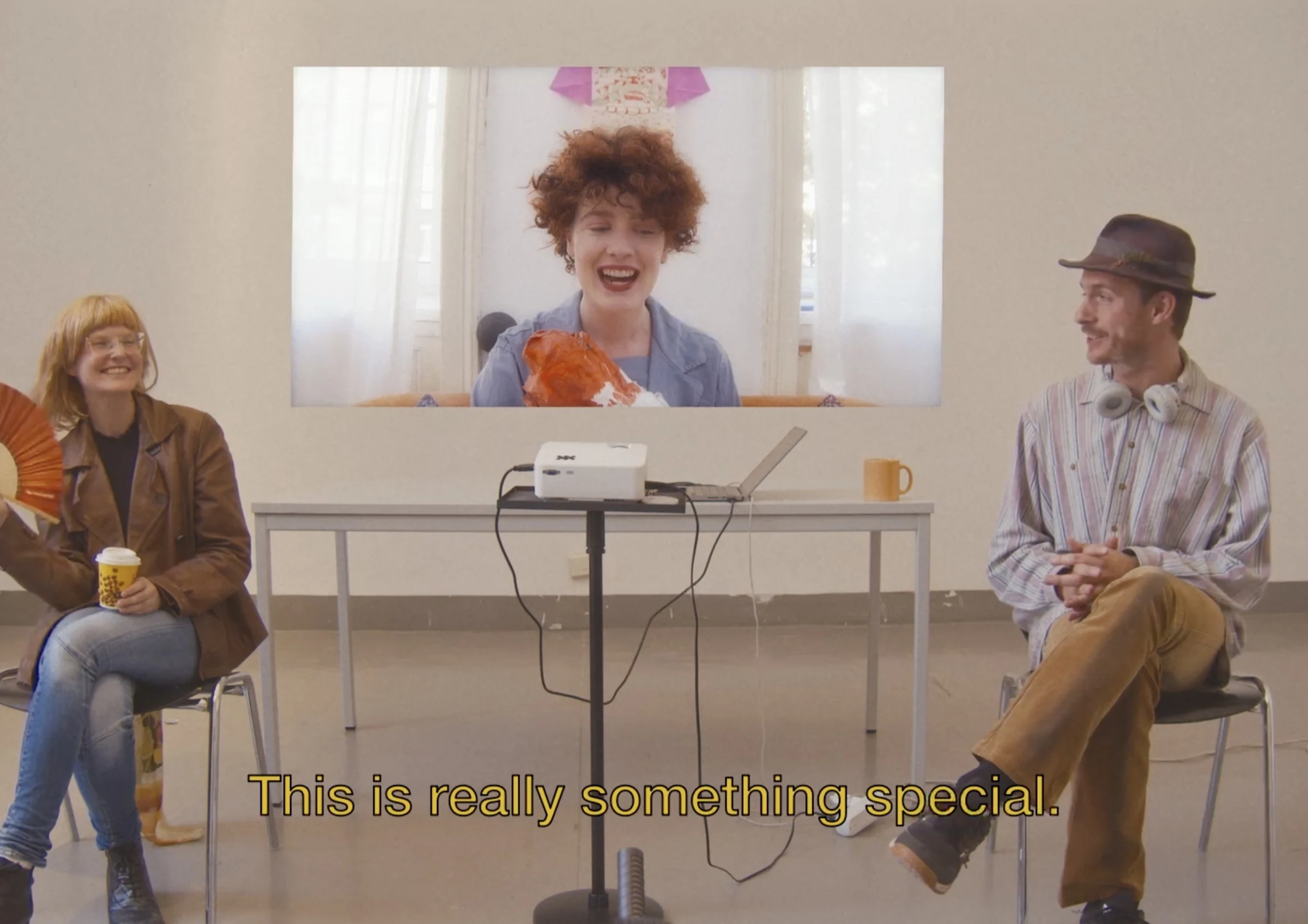 Two characters sitting beside a projection of a smiling character, subtitled This is really something special.
