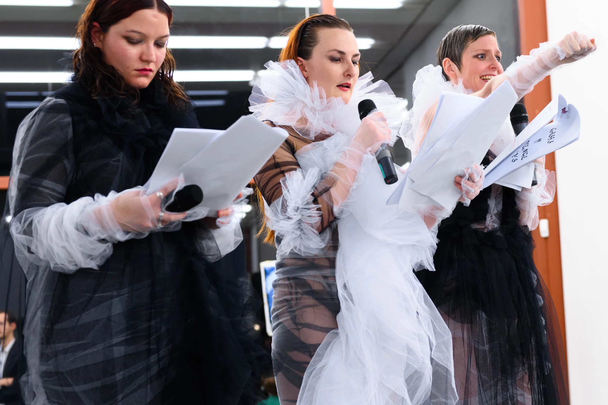 Three costumed performers reading scripts, with one gesturing towards the audience.