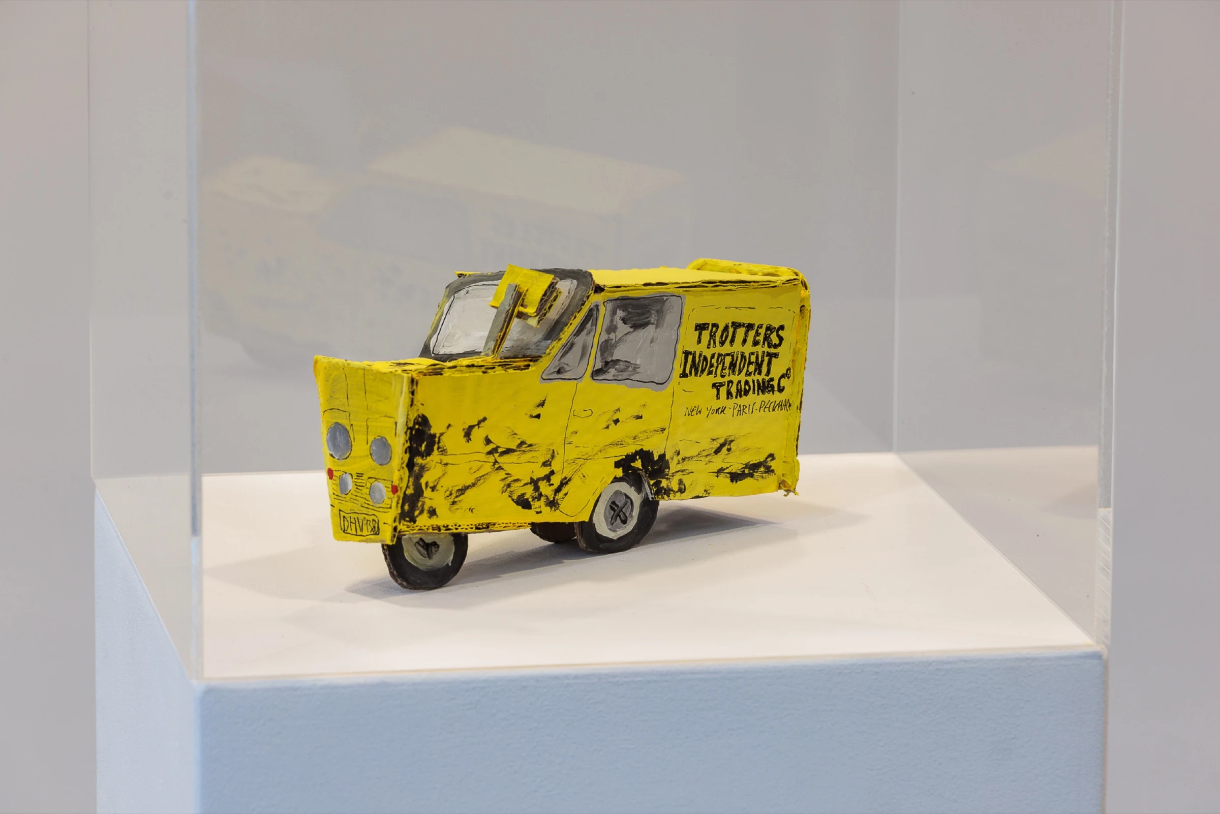 A yellow handmade cardboard Trotters Independent Traders van inside a transparent display case.