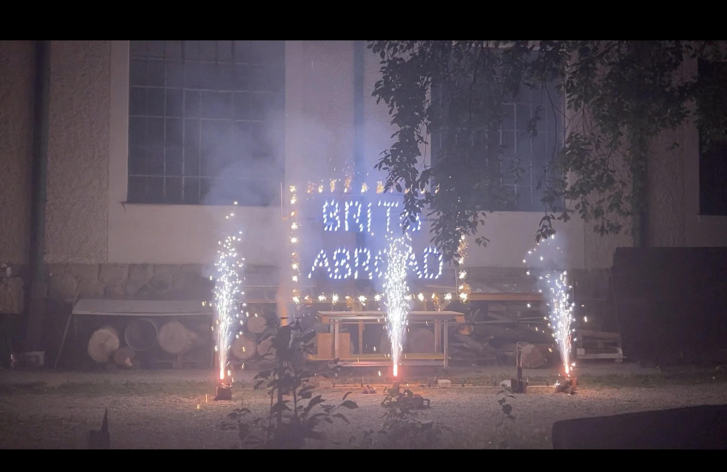 A wide view of three firework fountains surrounding the illuminated BRITS ABROAD sign.