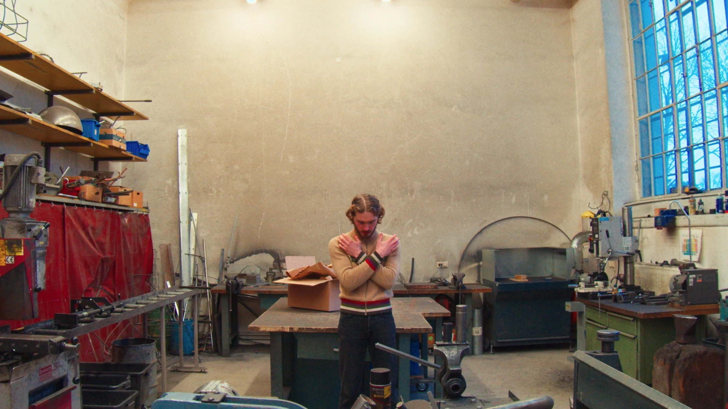 Young Man standing with his arms crossed over his chest in a metal workshop.