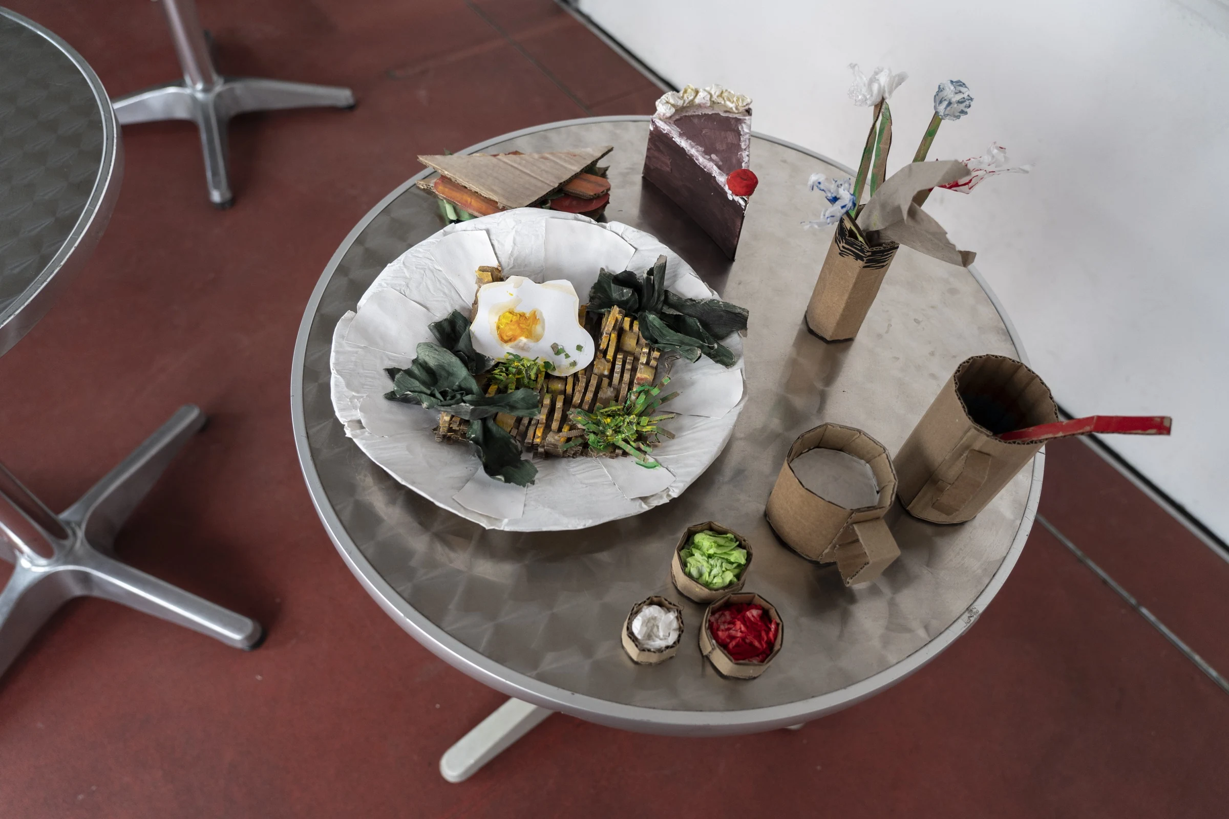 Finished cardboard food, cups and flowers arranged on a café table.