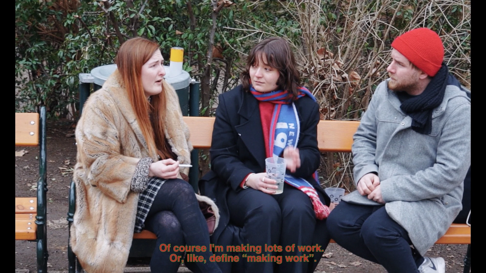 Three people talking on an outdoor bench in winter coats.