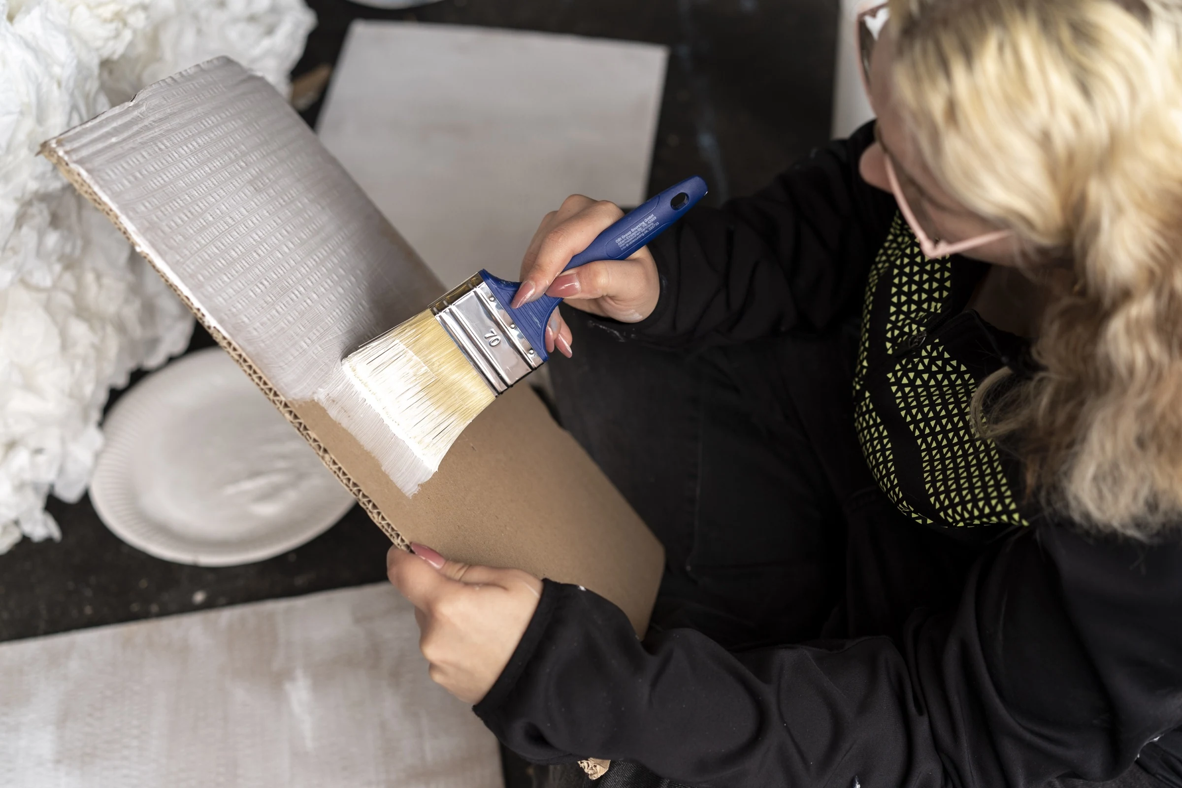 A participant painting a cardboard prop white with a wide brush.