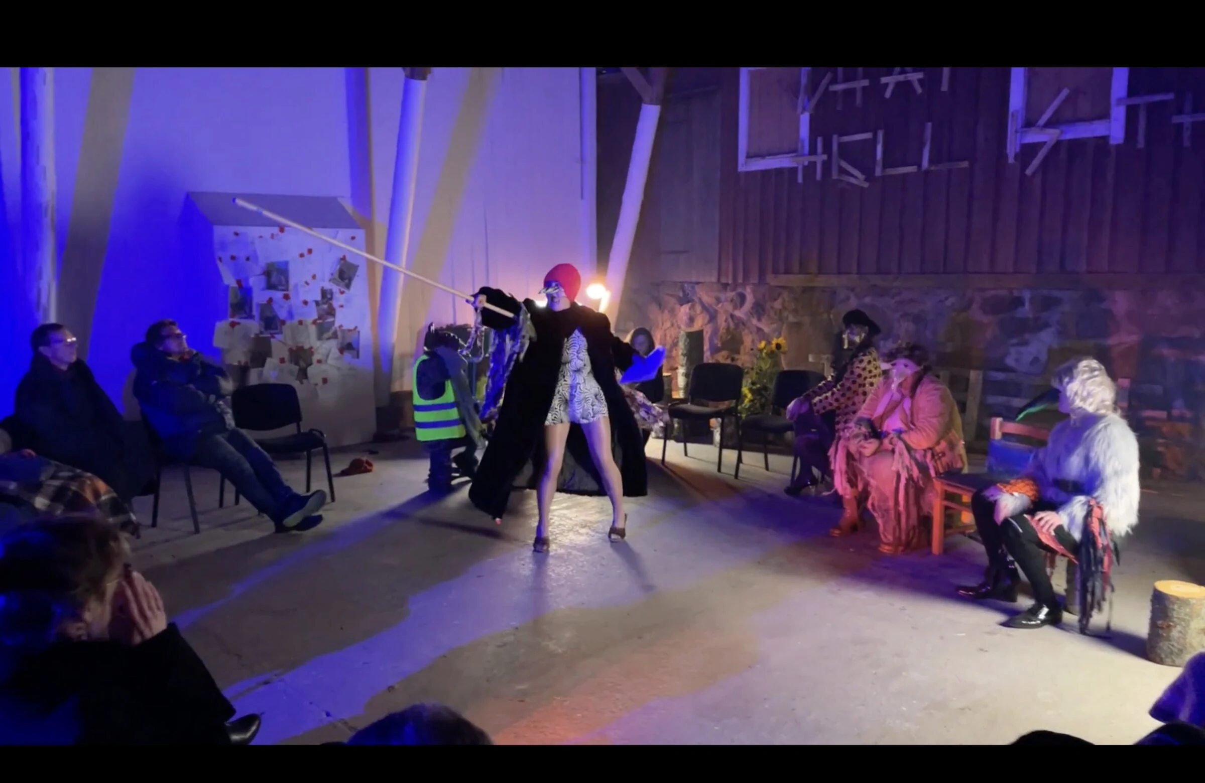 A performer pointing a long staff toward the audience in the barn.