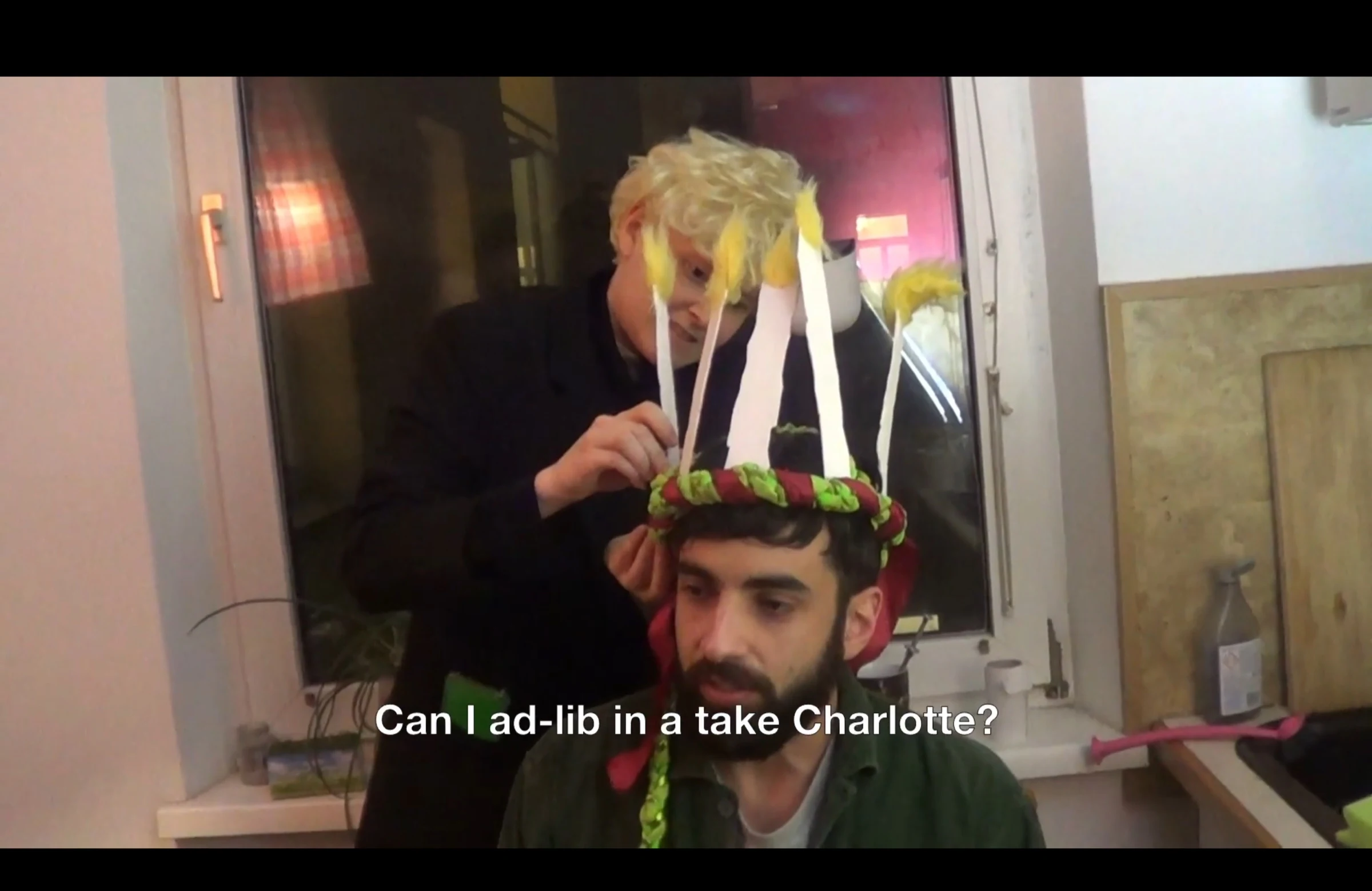 A crew member adjusts a handmade candle crown on a seated performer.