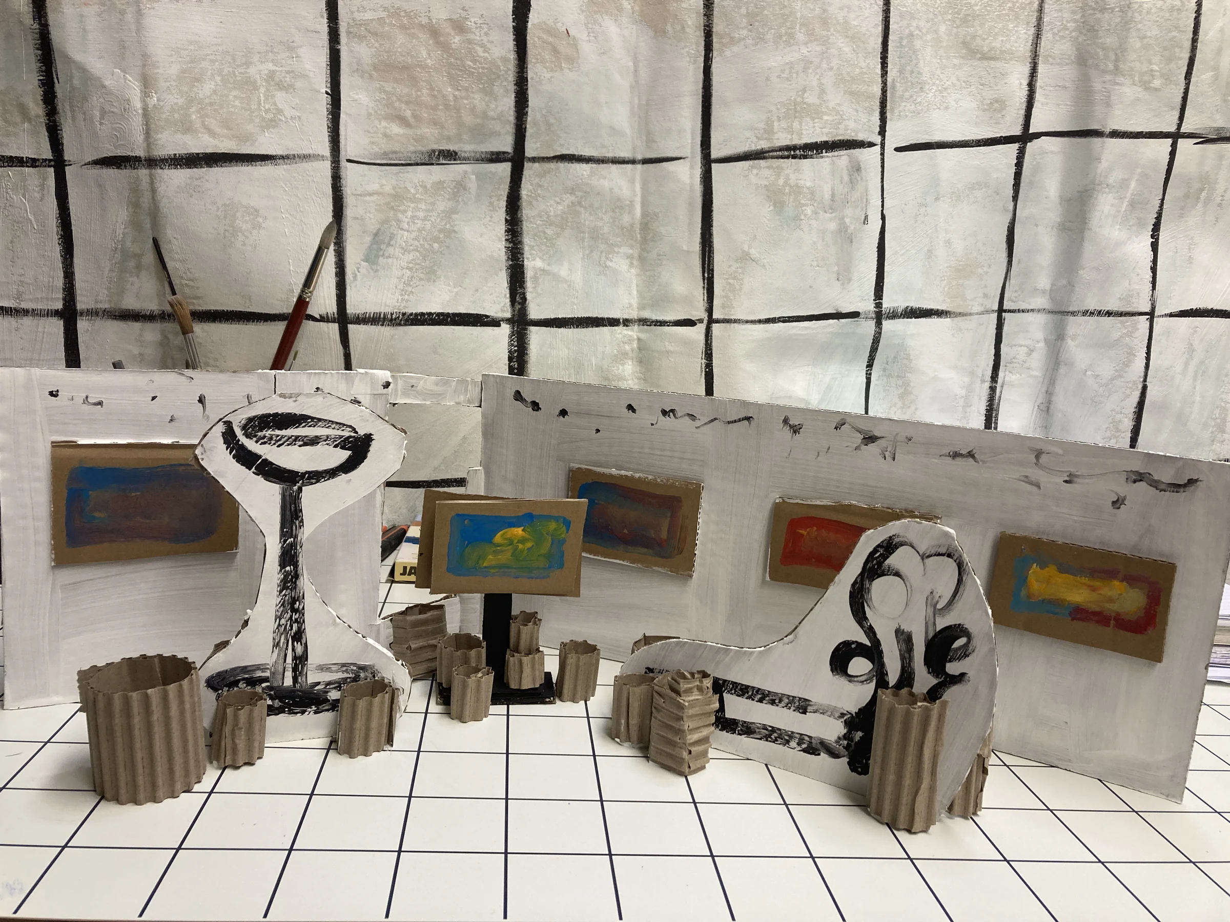A cardboard model of Location with painted sculptures, colourful miniature screens and a grid-patterned floor.