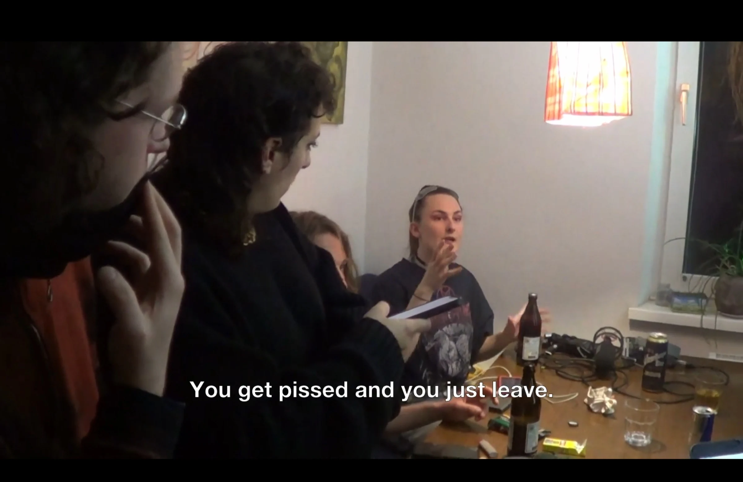Cast and crew discussing a scene around a kitchen table with bottles and recording equipment.