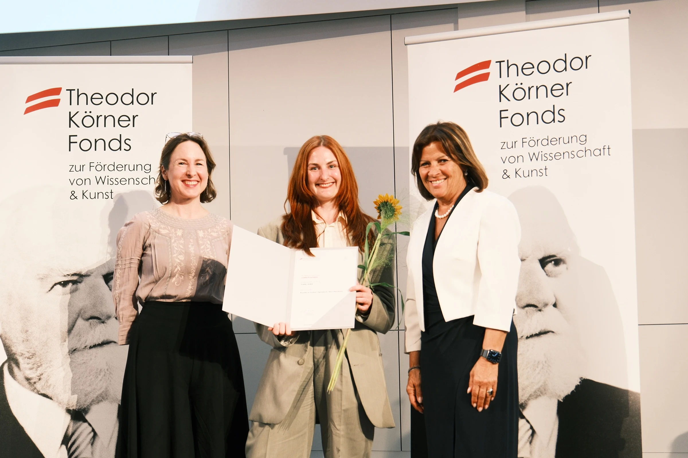 Charlotte Gash holding her prize certificate and a sunflower alongside two ceremony representatives.