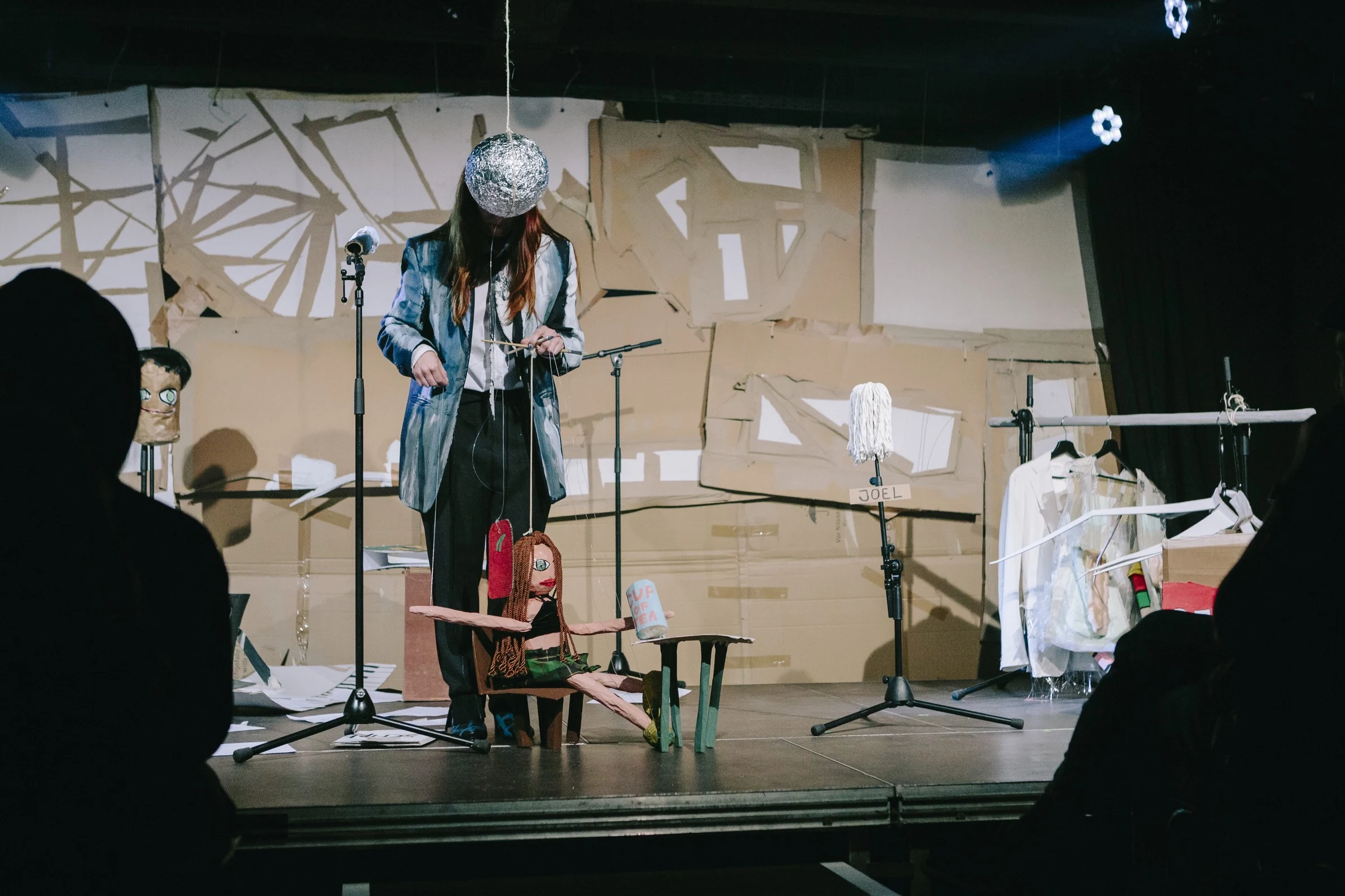 Charlotte Gash operating a handmade puppet on stage beneath a hanging silver ball.