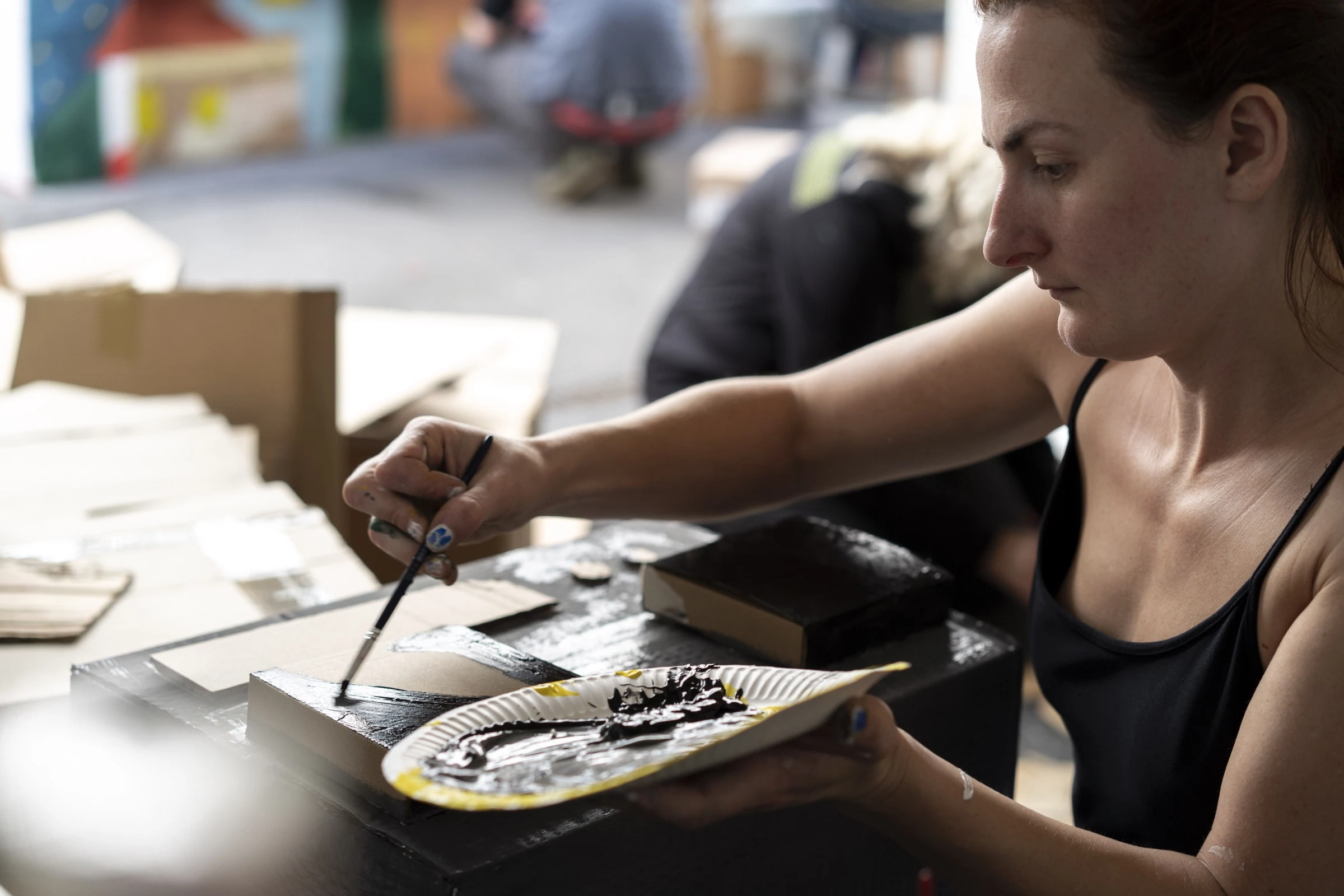 Close-up of Charlotte Gash painting a cardboard box black.