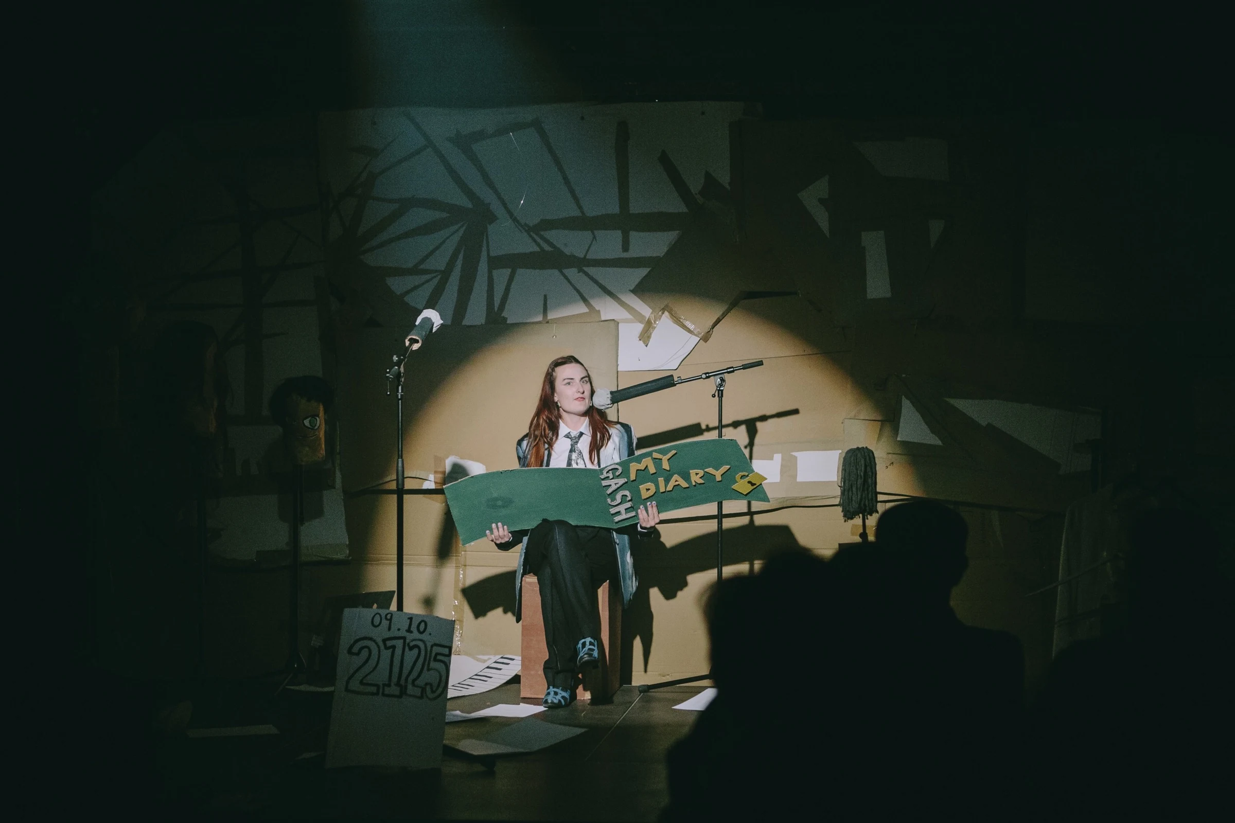 Charlotte Gash seated on stage holding a large green cardboard diary.