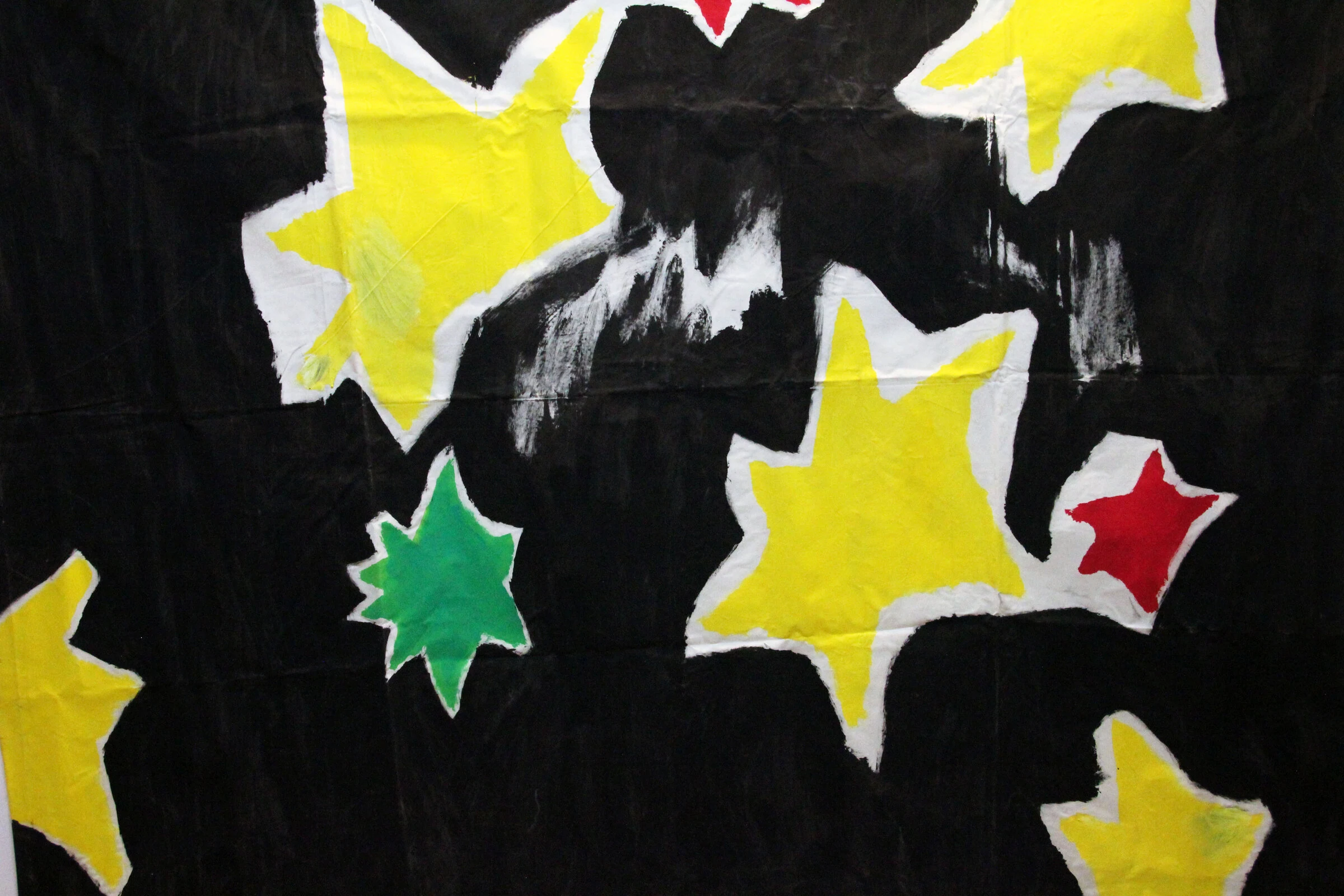 A detail of a black canvas backdrop with yellow, green and red stars outlined in white.