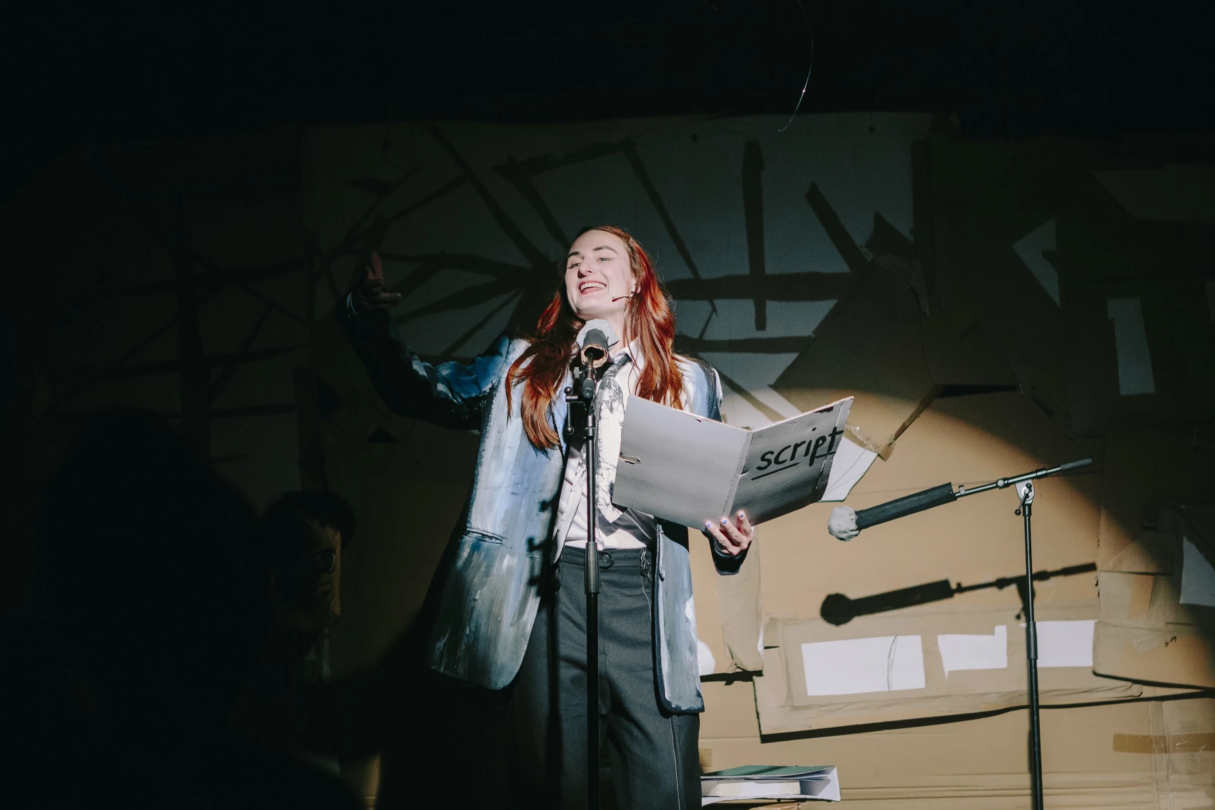 Charlotte Gash reading a script at a microphone on a cardboard stage.