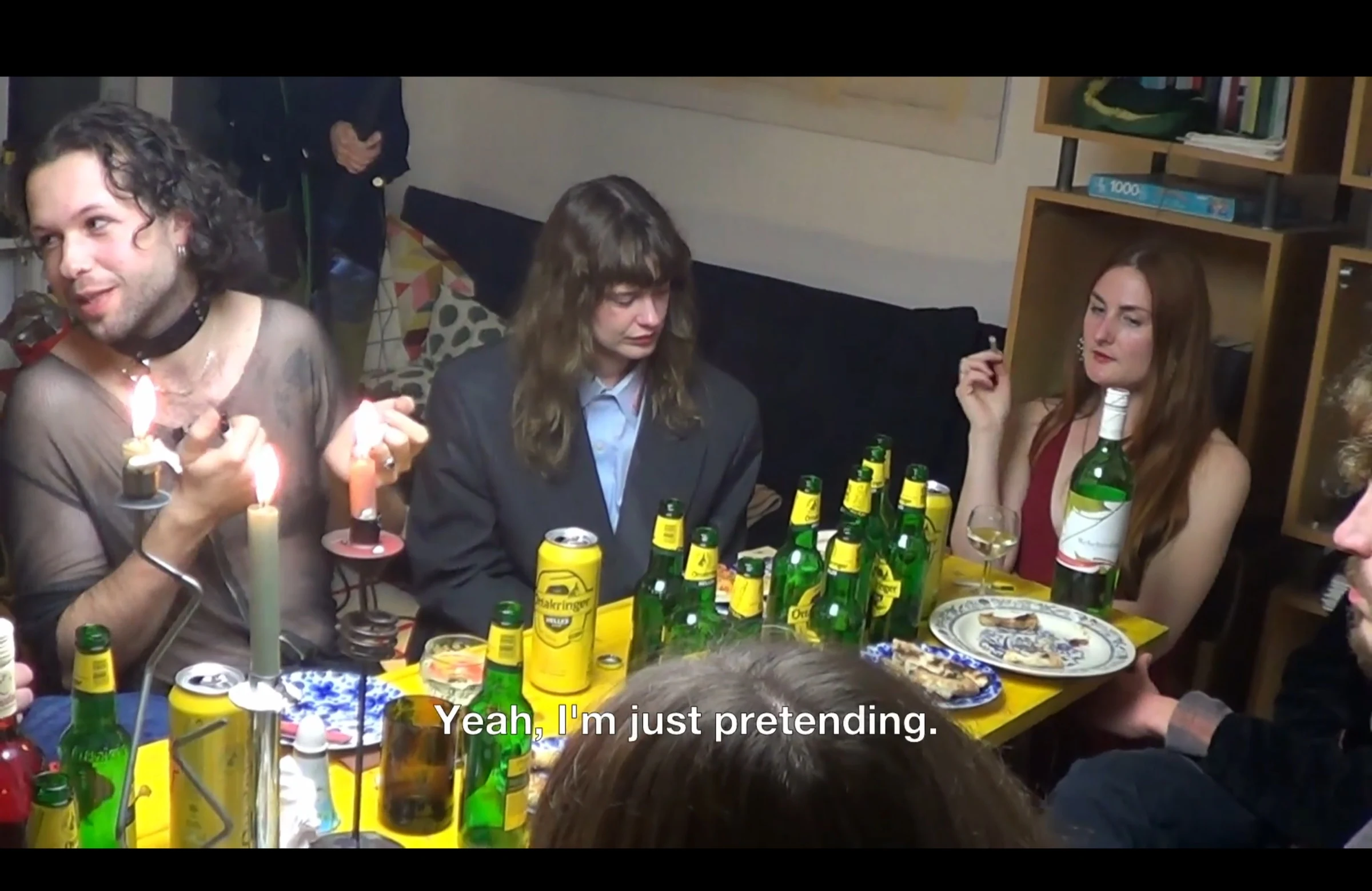 Performers gathered around a yellow table filled with bottles, plates and lit candles.