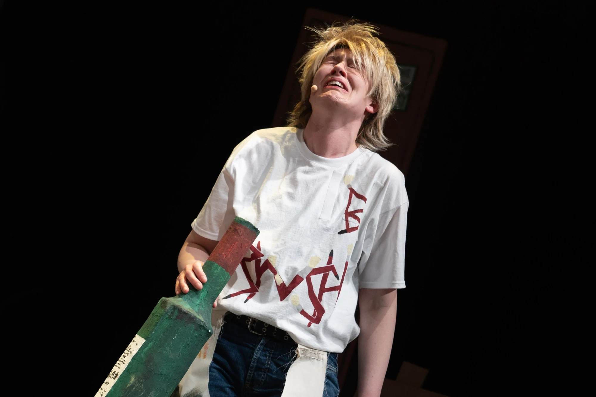 A performer in a blond wig holding an oversized cardboard bottle.