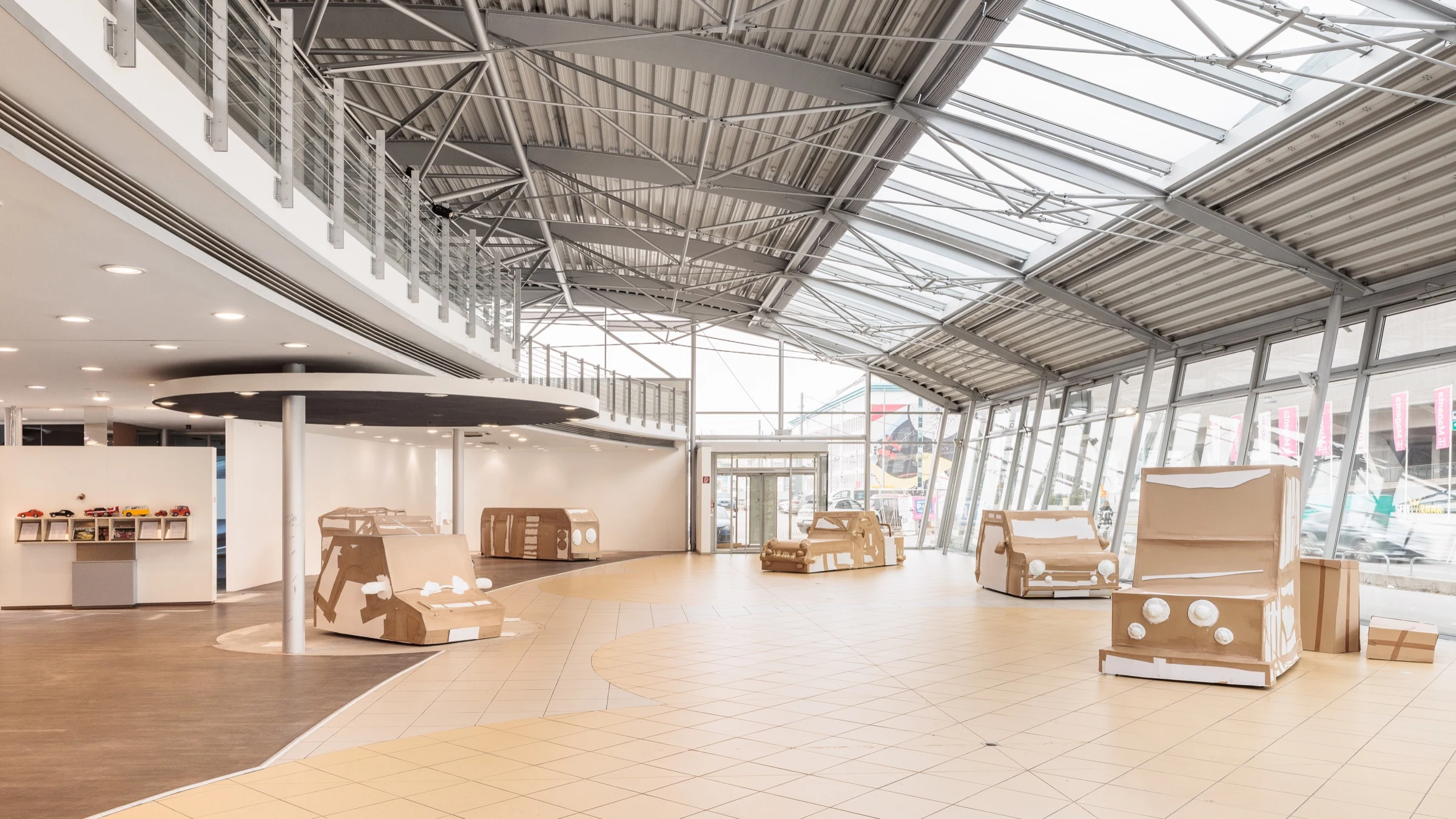 Full-size cardboard vehicles displayed throughout a bright former car showroom.