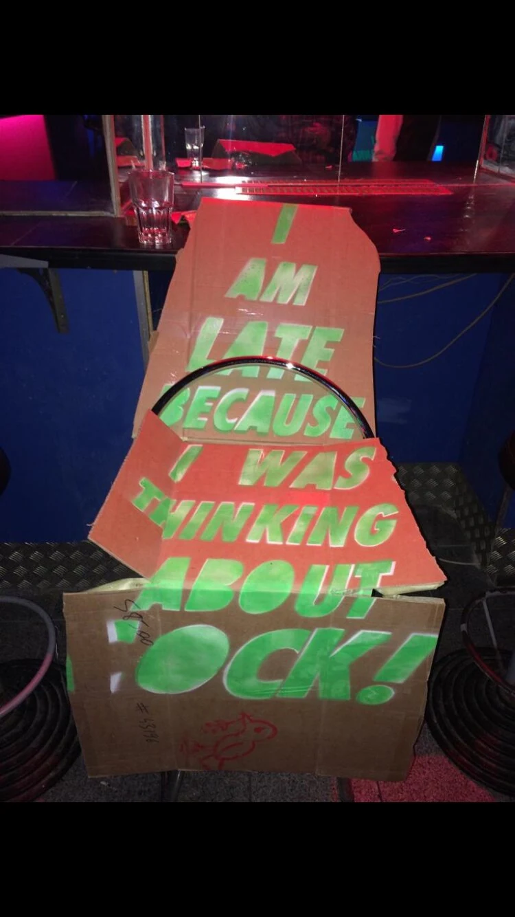 A cardboard dress with green lettering arranged on a bar stool.