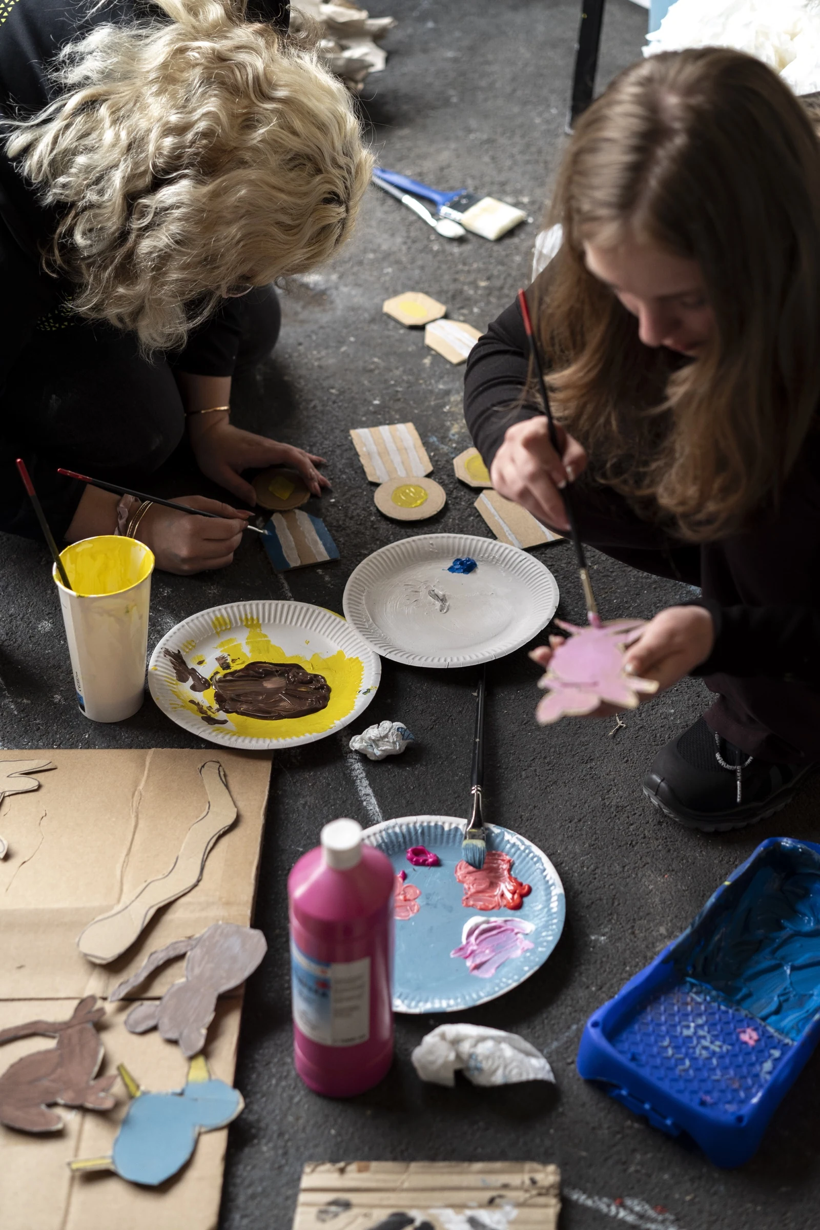 Two participants painting cardboard animal cutouts on the floor.