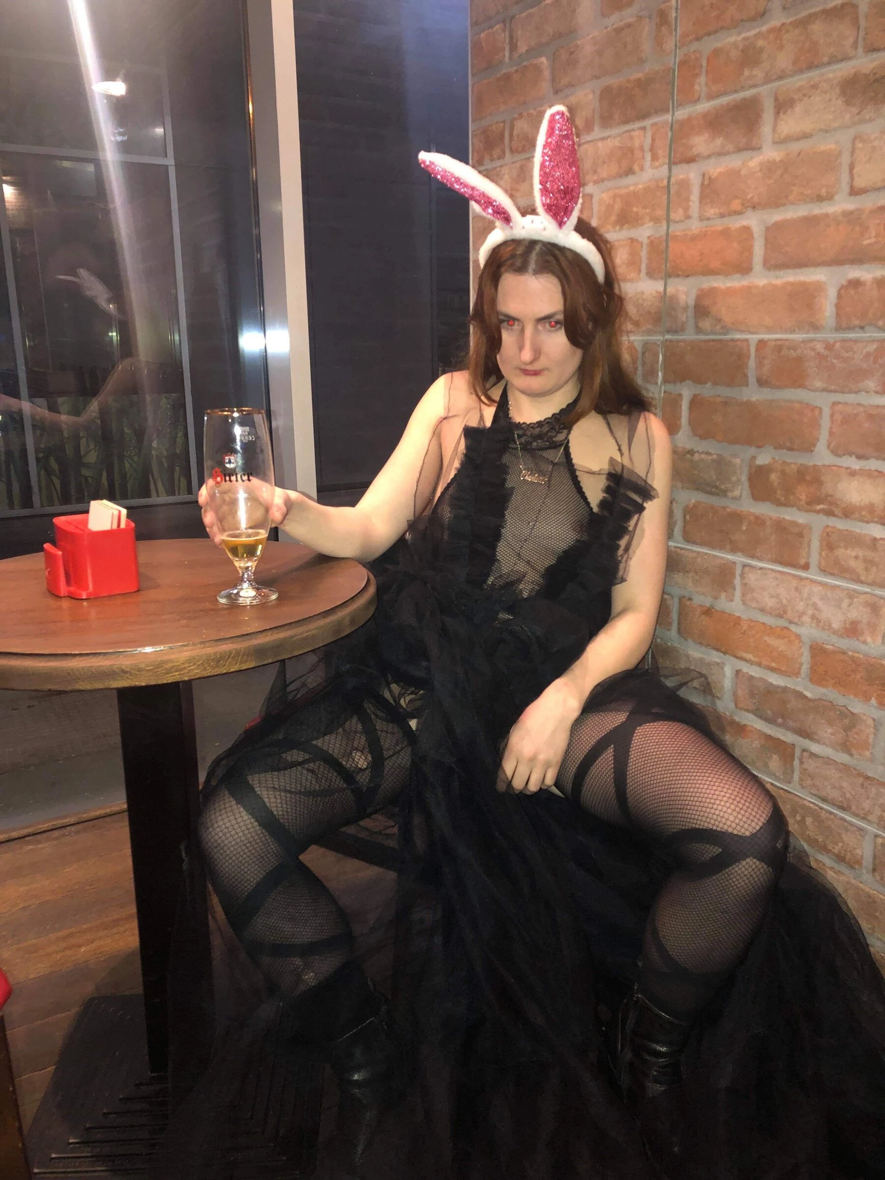 A performer in a black tulle costume and pink rabbit ears seated with a beer.