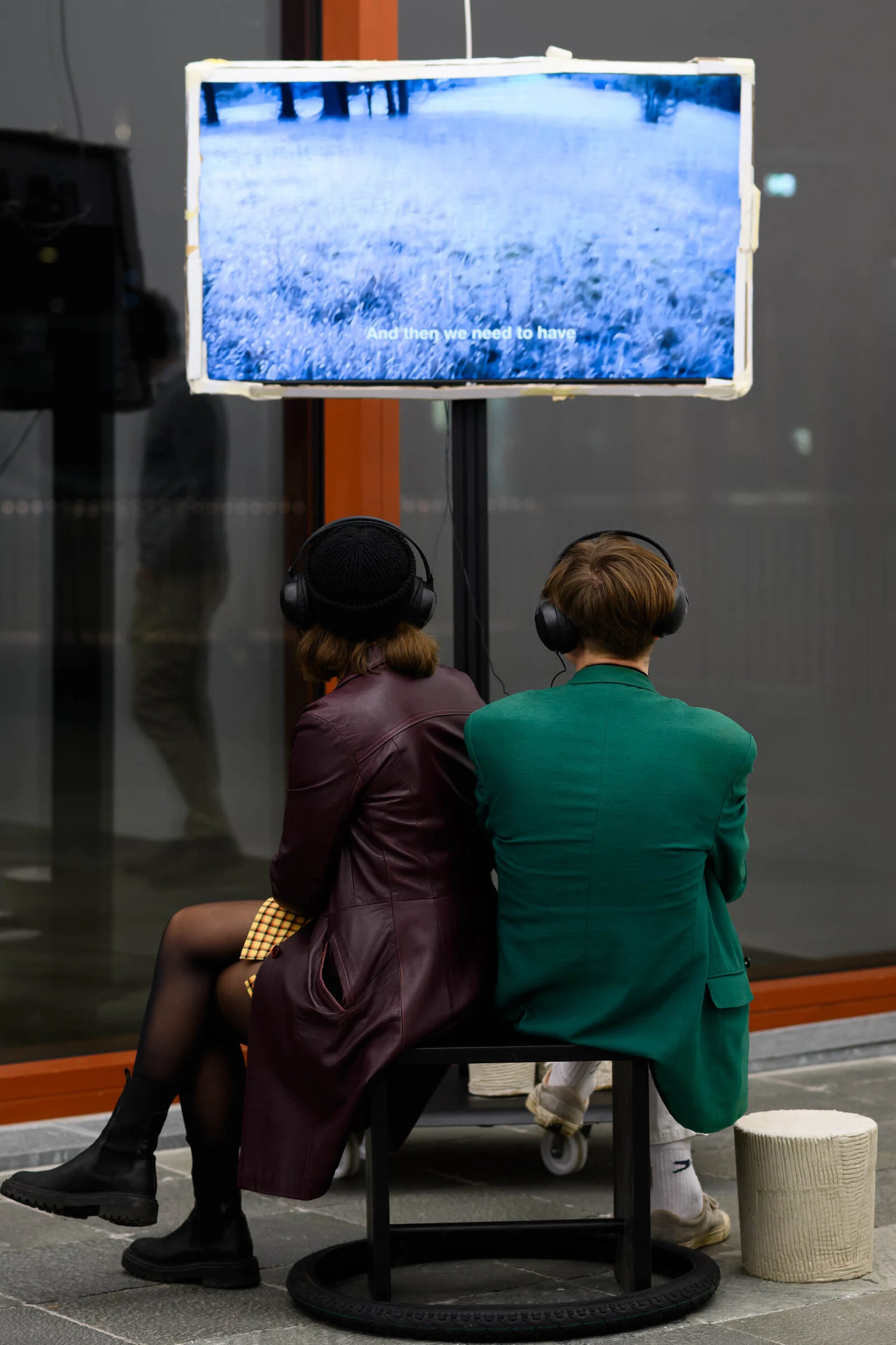 Two visitors sitting back to back wearing headphones and watching a snowy landscape on a LOCATION video screen.