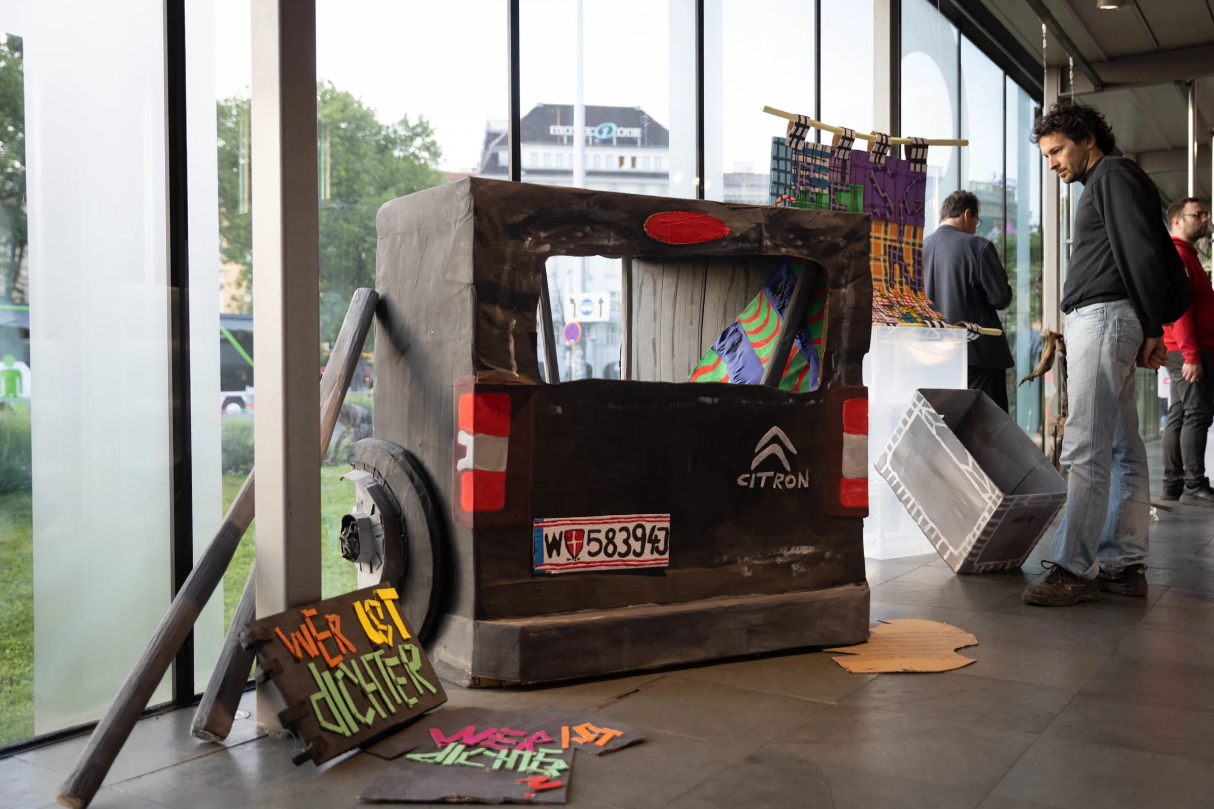 Visitors viewing a cardboard Citroen van and handmade signs inside the gallery.