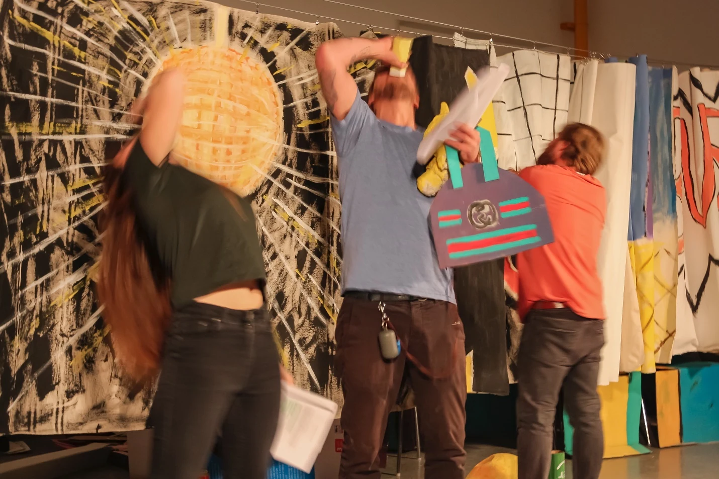 Three performers with scripts and a cardboard shopping bag in front of a painted disco ball.