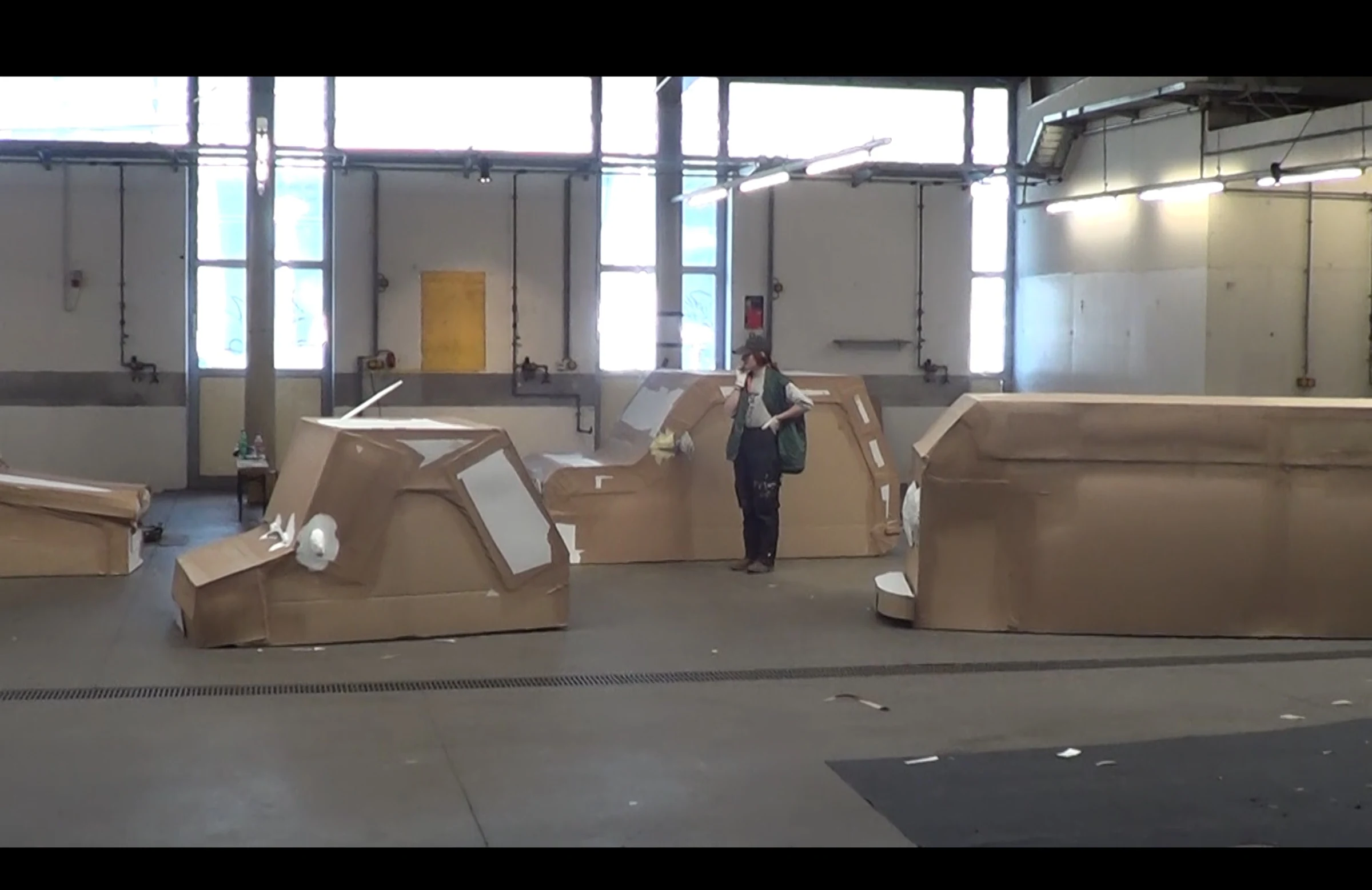 Charlotte performing among full-size cardboard vehicles in an industrial space.