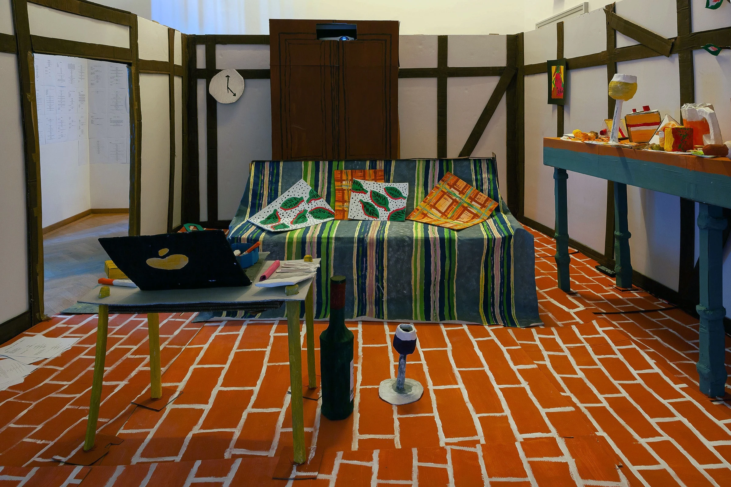 The cardboard apartment installation with a striped sofa, low table and painted brick floor.