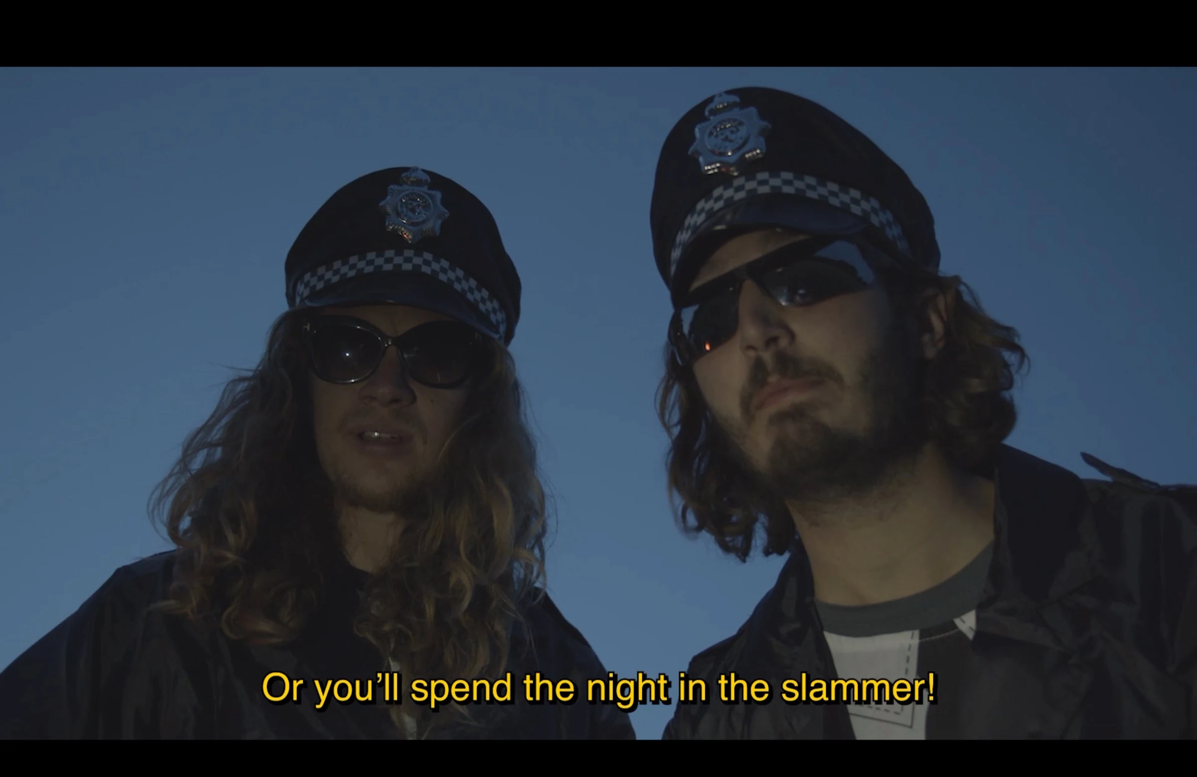 Two characters in police costumes and sunglasses against a blue evening sky.