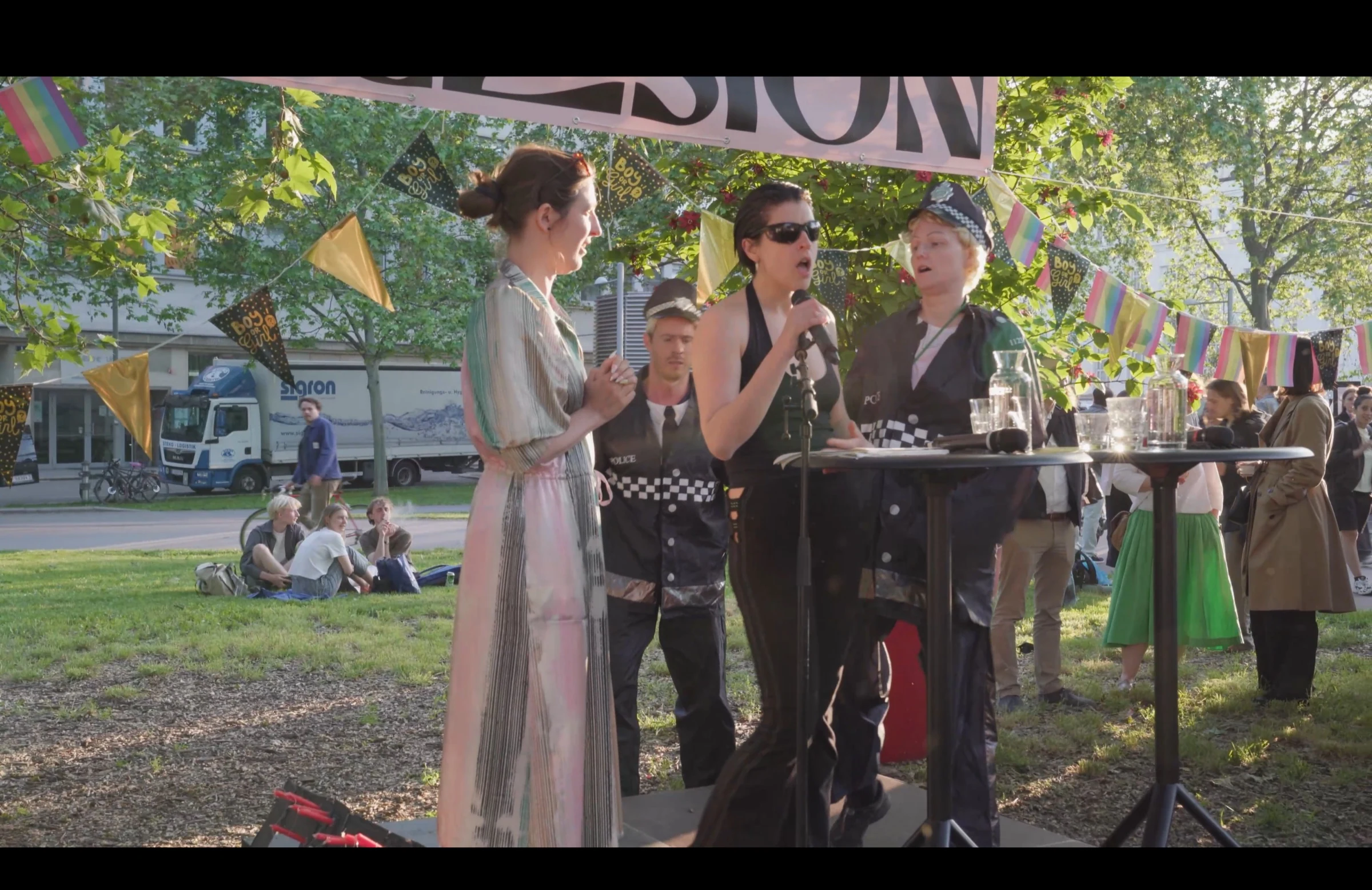 An outdoor award ceremony with a speaker at a microphone and performers in police costumes.