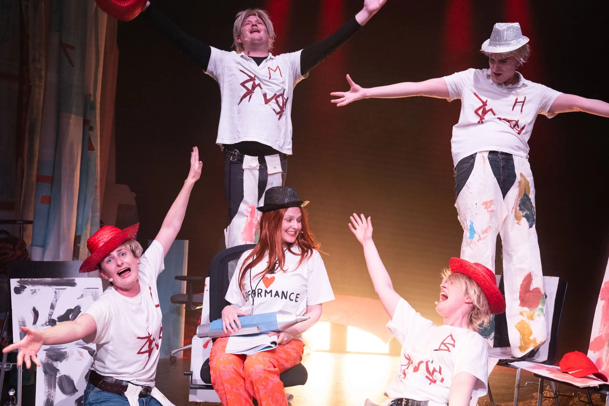 Five performers in sparkling hats posing with raised arms around Charlotte on stage.